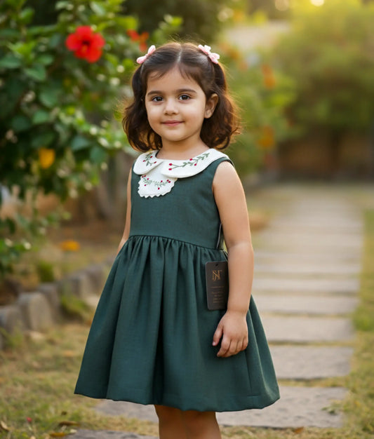 Baby girl wearing the festive green linen dress with embroidered Peter Pan collar.