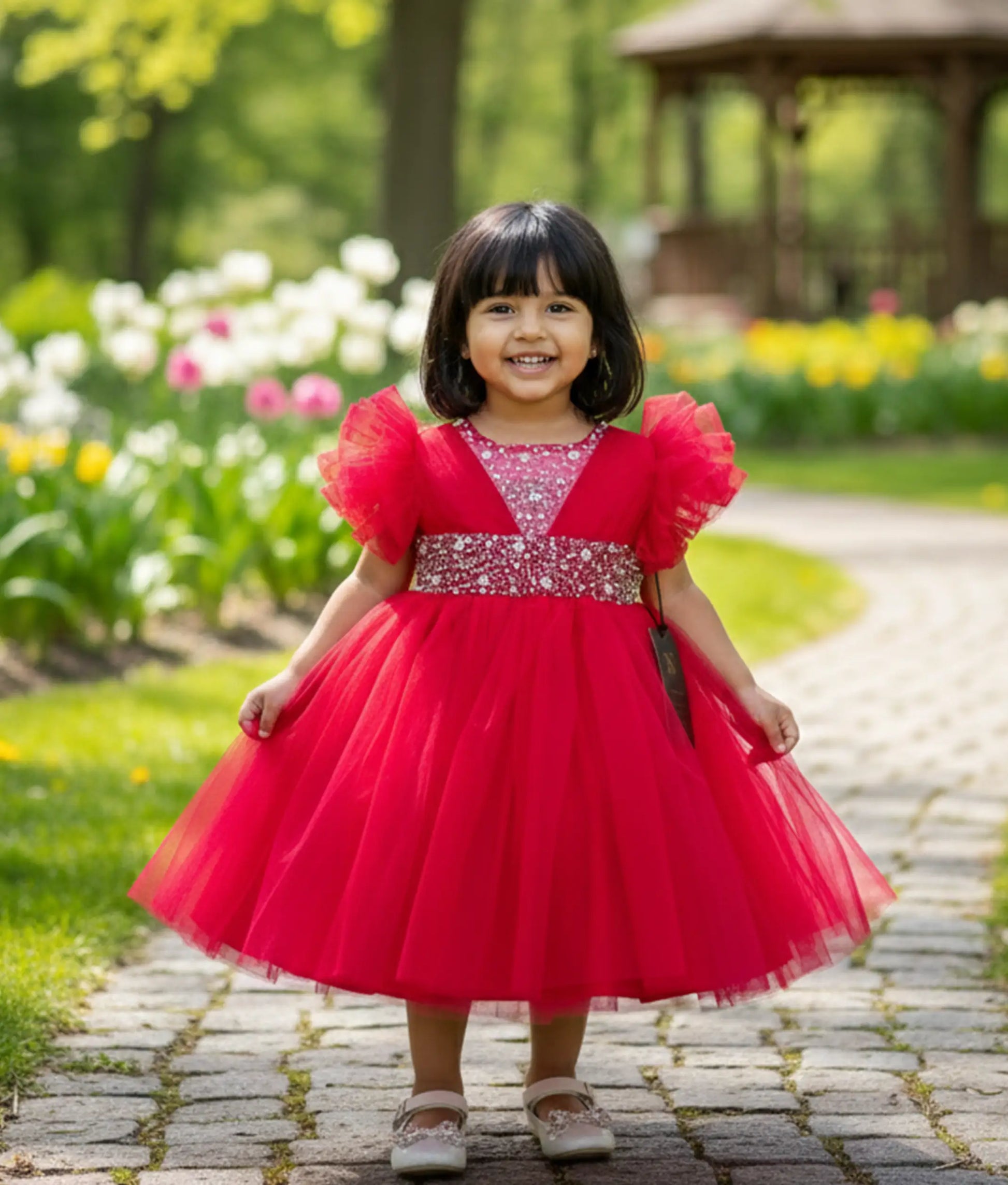 A baby girl wearing a hot pink handworked tulle net birthday frock with butterfly sleeves and a layered flare.