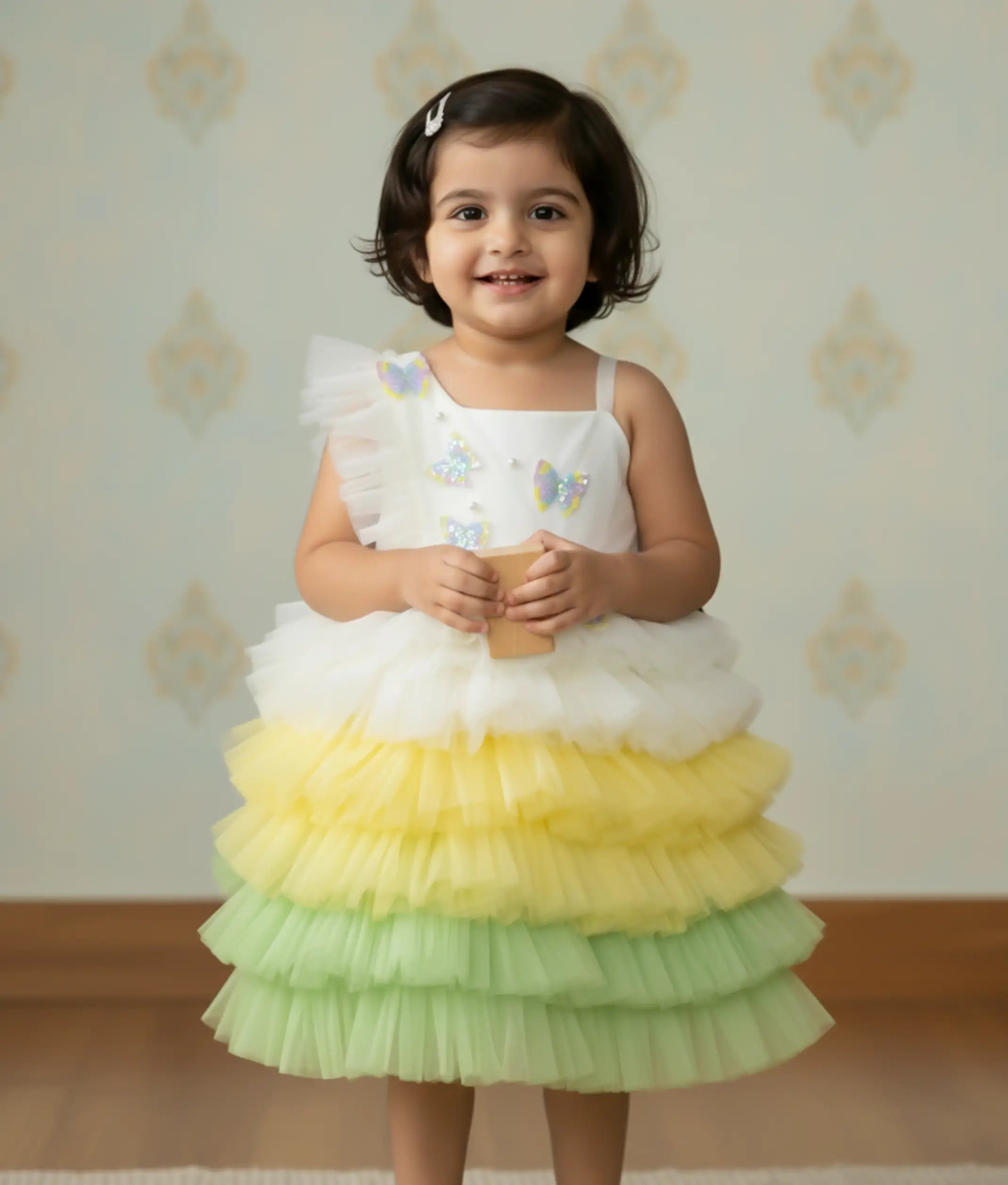 A baby girl wearing the multi-color tulle net butterfly-themed birthday frock, showcasing the fit, one-shoulder frill, and tiered step-net skirt.