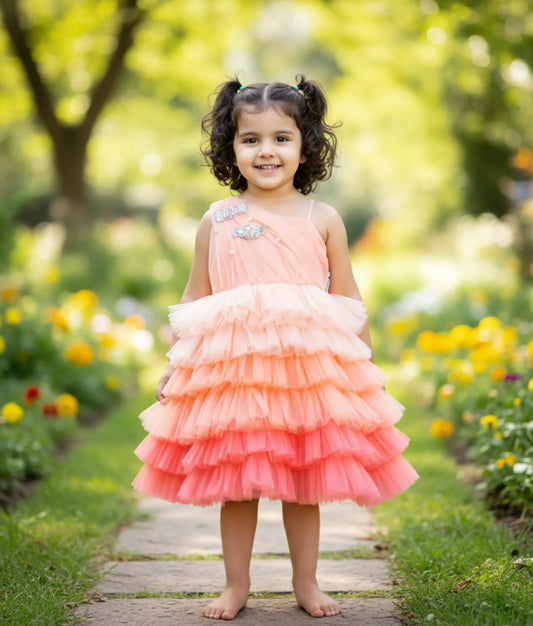 A baby girl wearing the peach candy-themed birthday frock, showing the asymmetric one-shoulder fit and ruffled step-net skirt.