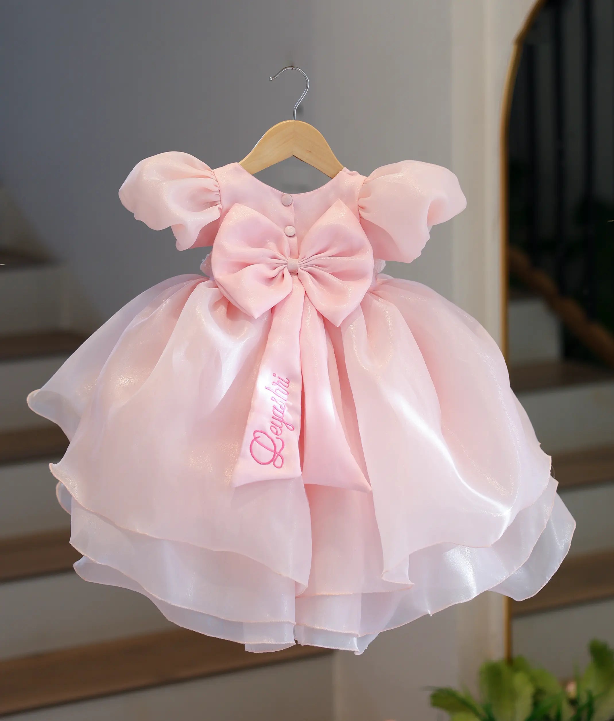 Back view of the baby pink birthday frock featuring a large statement matching fabric bow with a personalized name embroidery on the trailing ribbon.