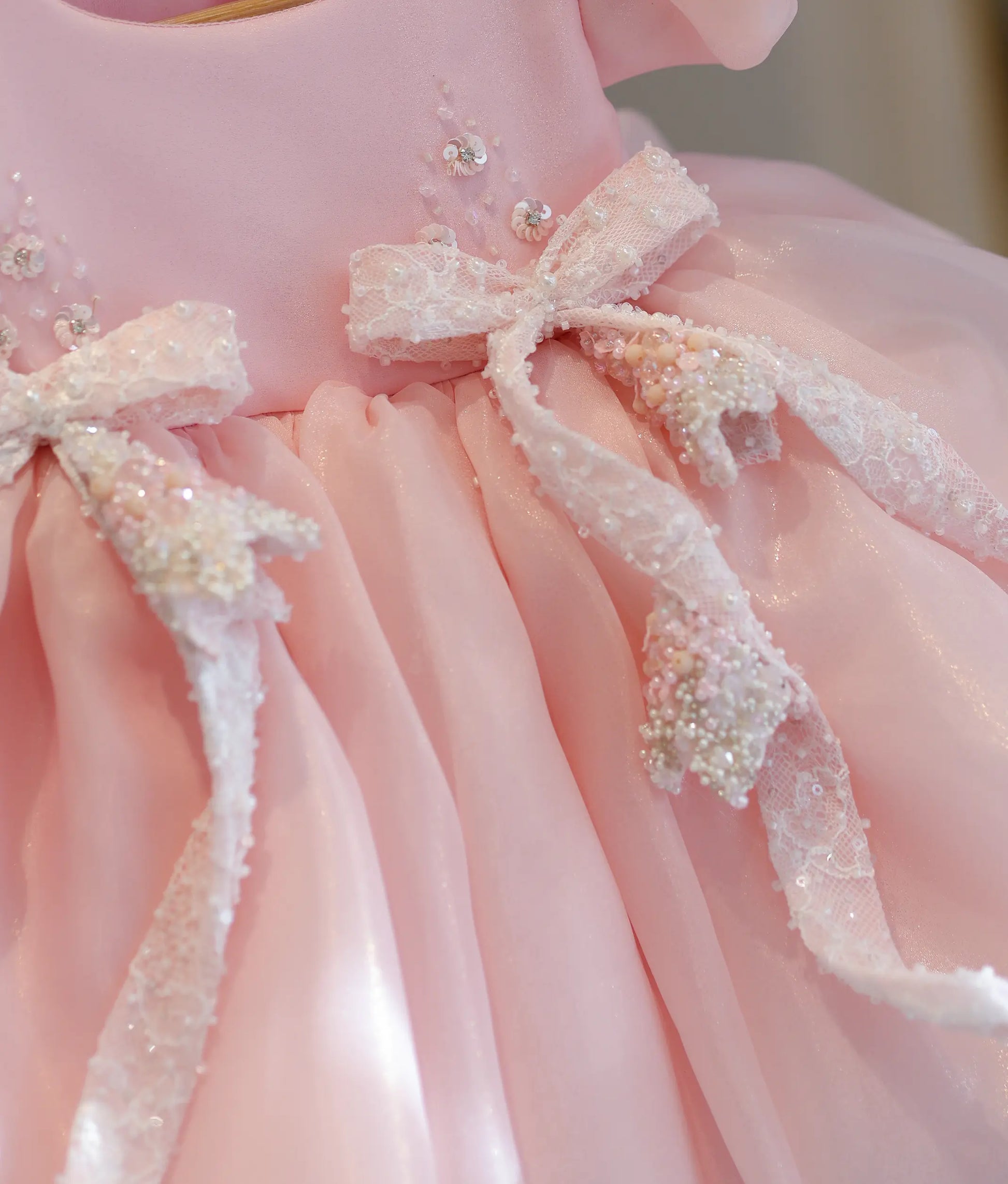 Detailed close-up view showing the intricate beadwork, sequins, and texture of the elegant lace bows on the baby pink birthday dress.