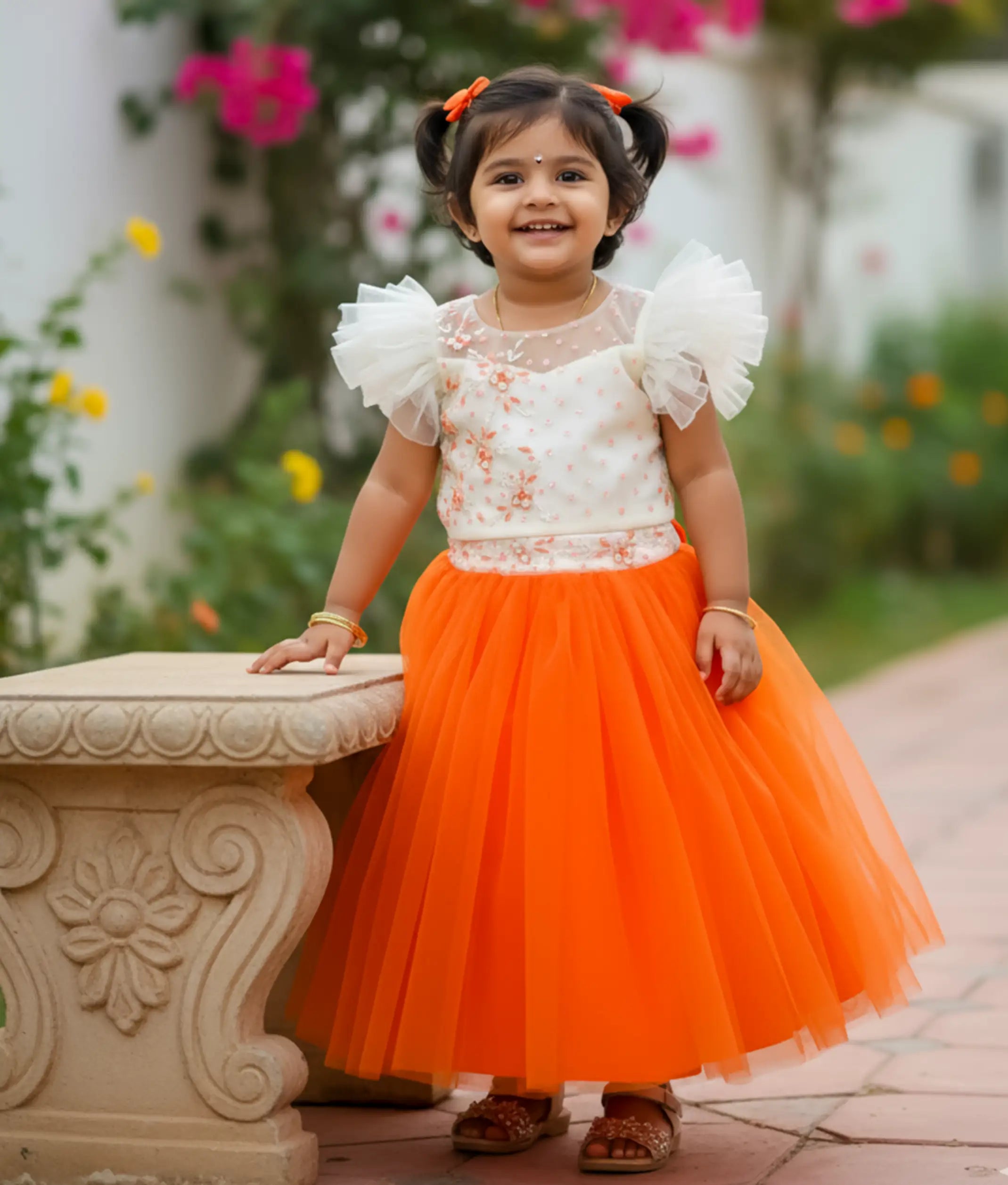 baby girl wearing a off-white handworked top and orange tulle skirt
