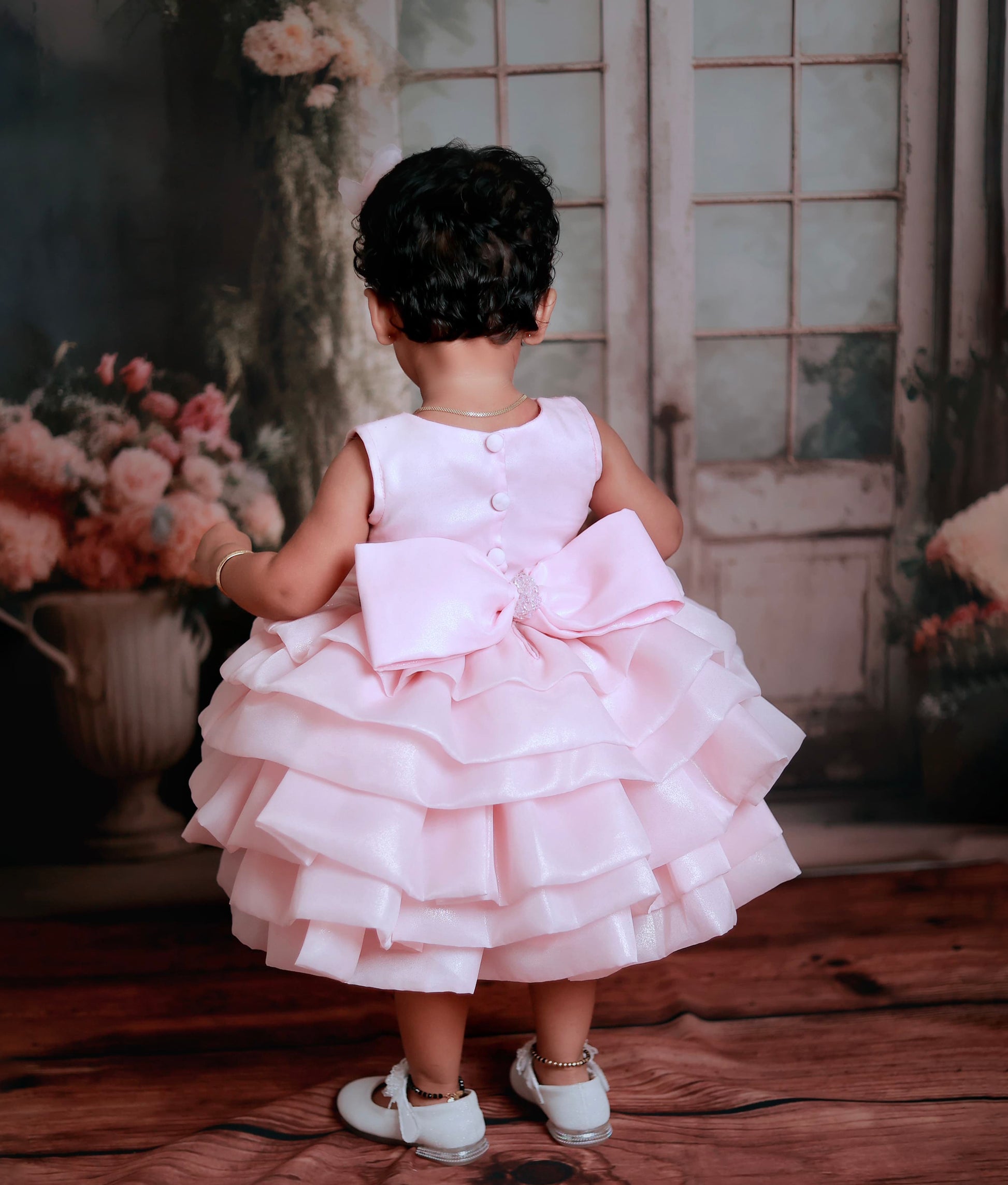 Back view of the pink shimmer organza frock featuring a V-neckline and a decorative bow with a crystal centerpiece.