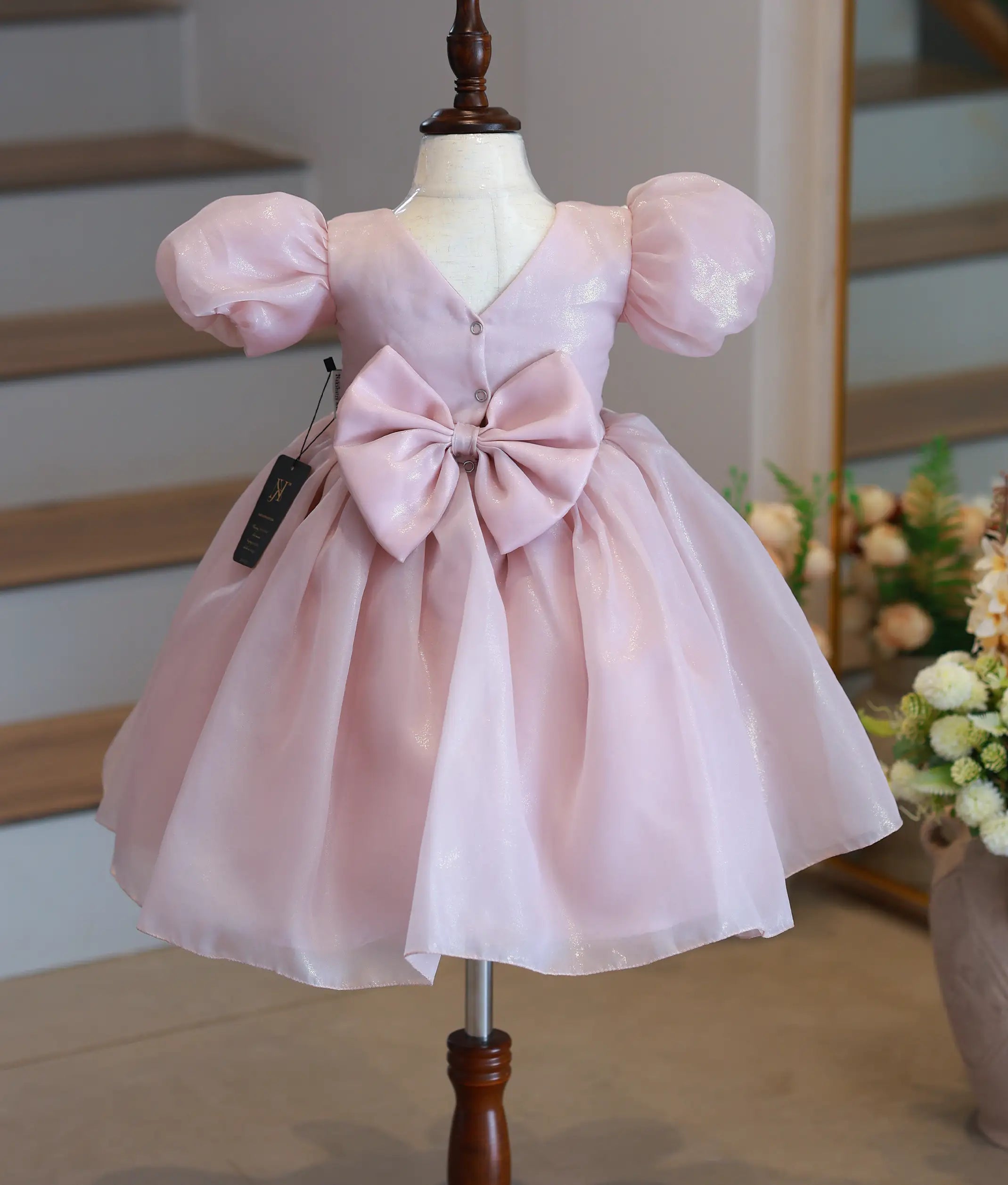 Back view of the dusty pink shimmer organza frock featuring a v-neckline, button closure, and a decorative bow.