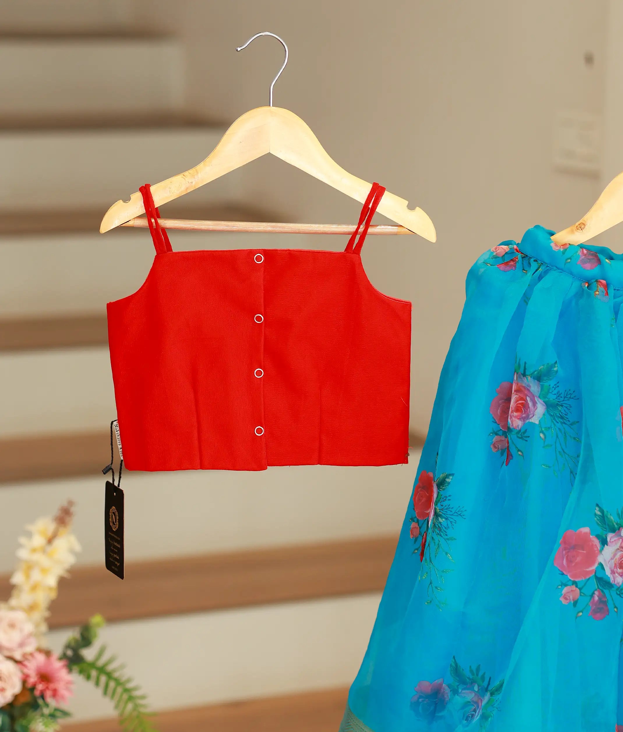 The back view of the red top showing the square neckline and press-button closure, displayed alongside the blue printed fabric