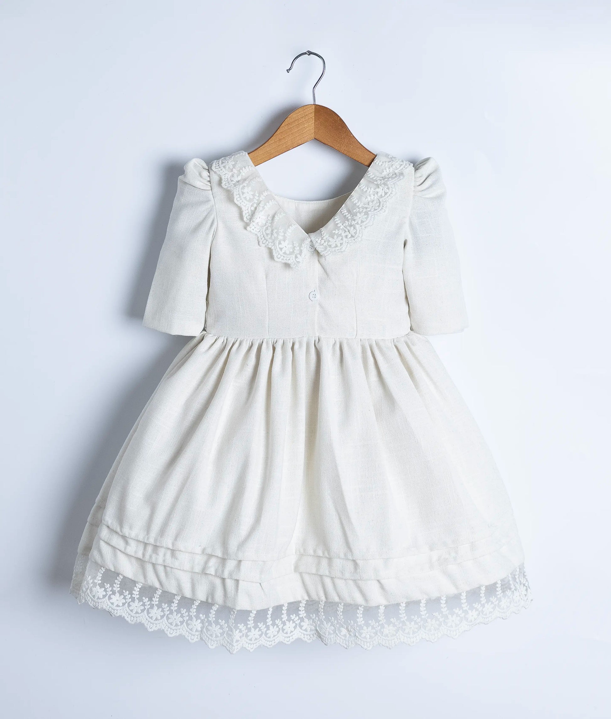 Back view of the off-white dress, clearly showing the V-neck with lace trim and the button closure detail.