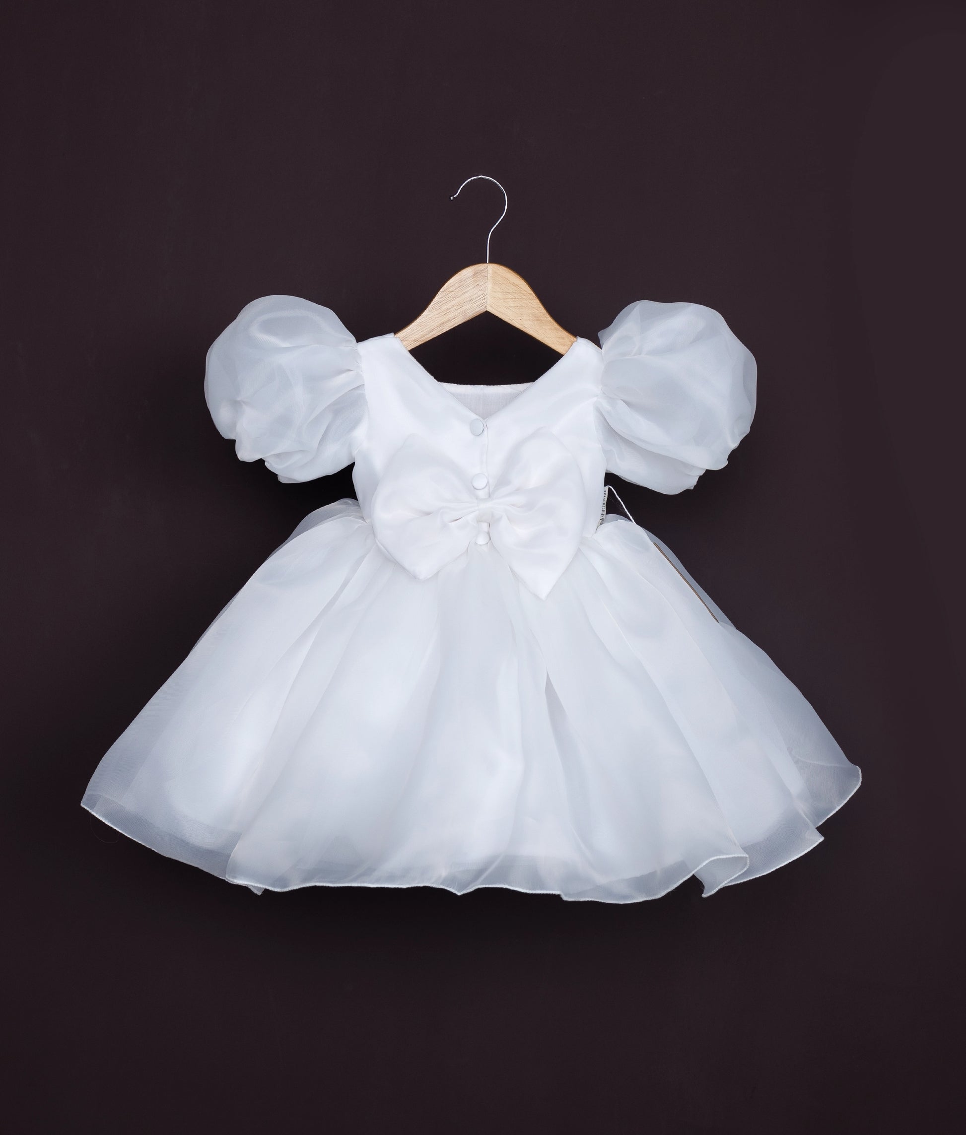 Close view of an off-white baby girl dress with puff sleeves and floral waistband—perfect for birthdays and special occasions