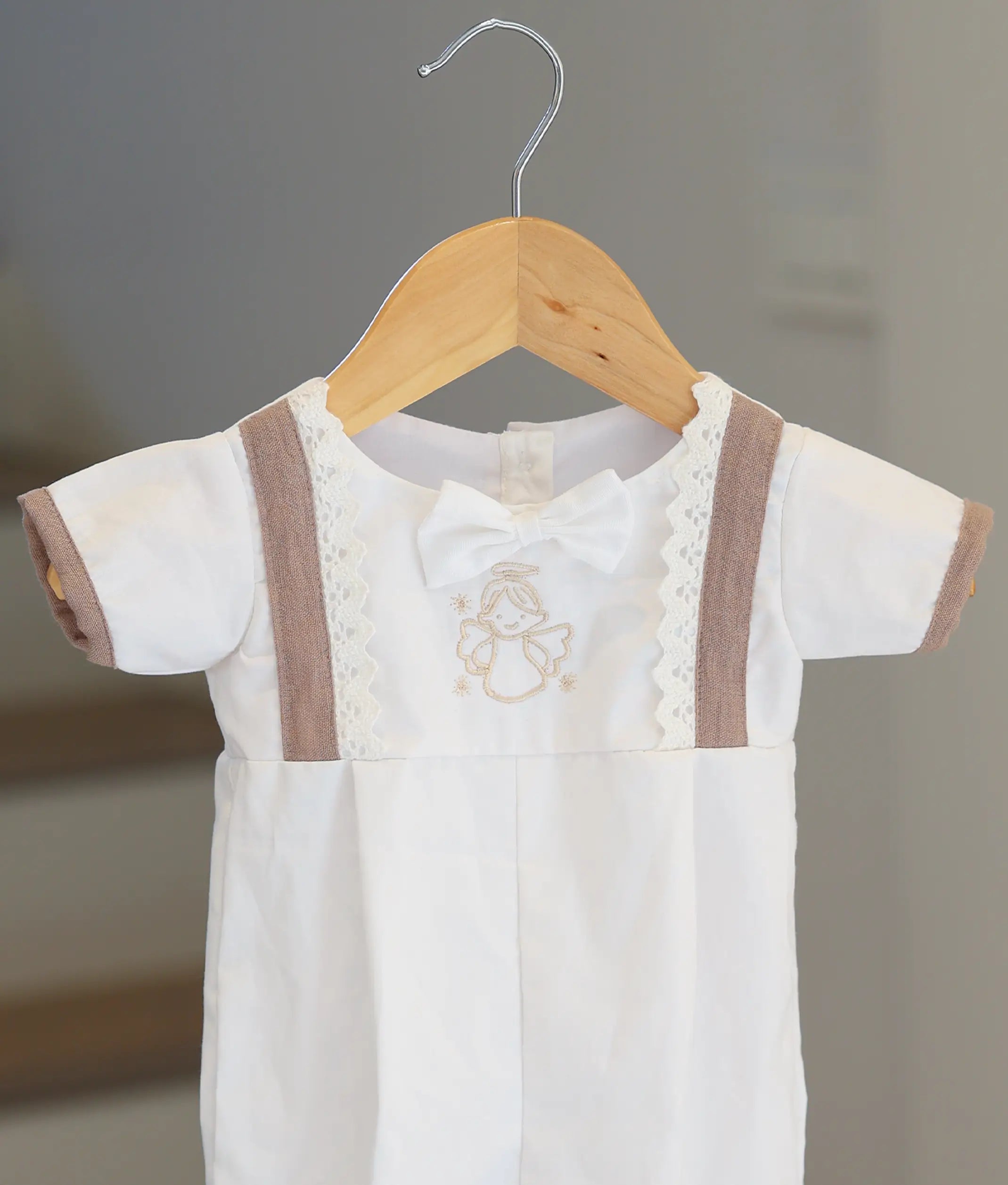 Close-up of the hand-stitched angel and beige lace details on the baby boy romper.