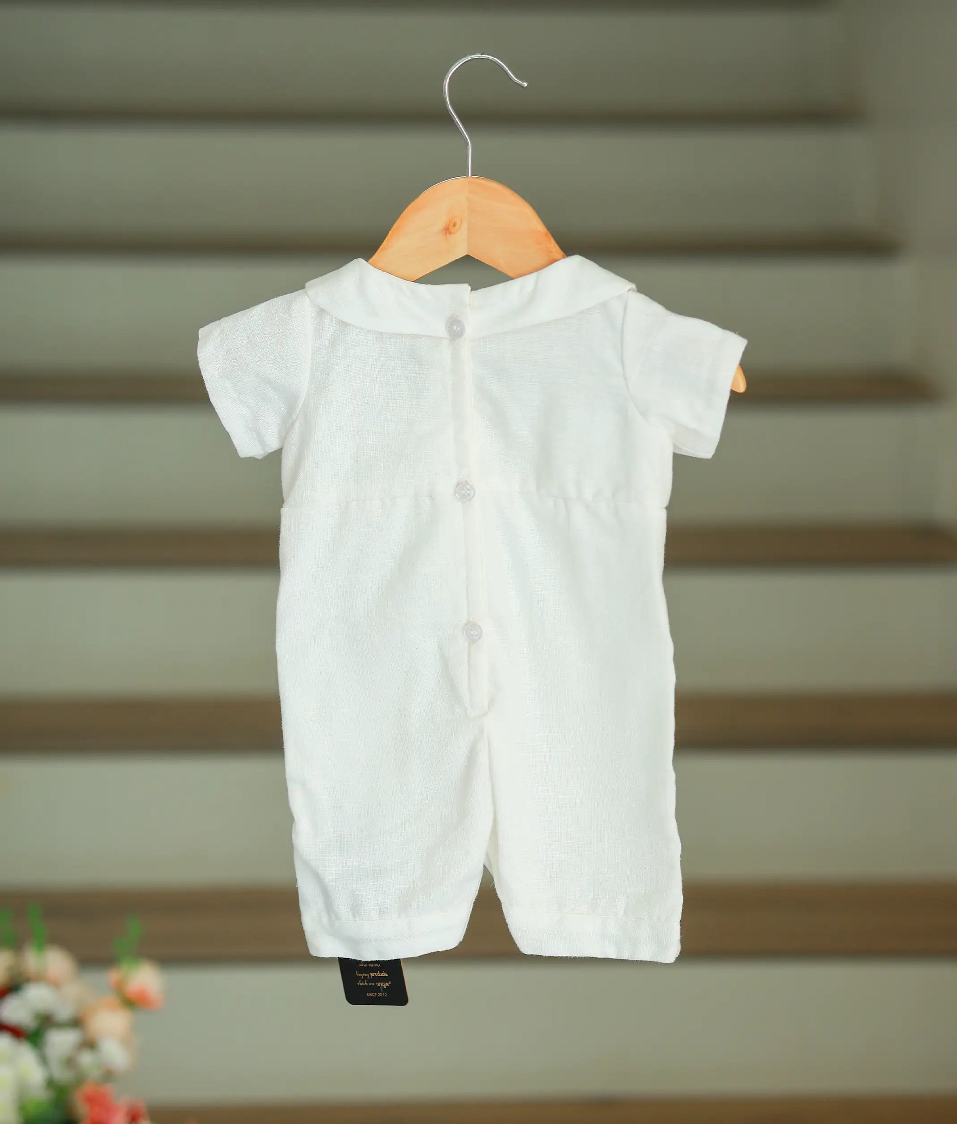 The back view of the off-white baptism romper showing the full-length white button closure for easy wear