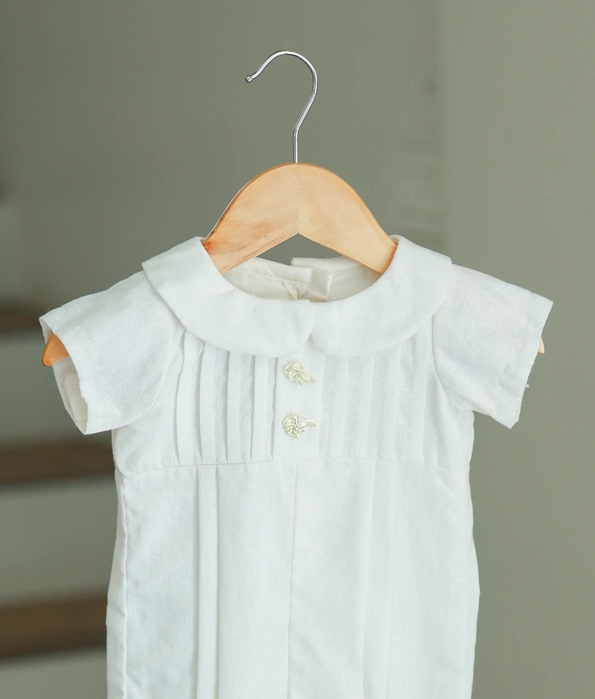 Close-up of the baby romper's bodice showing the intricate vertical pleating, Peter Pan collar, and delicate floral button accents