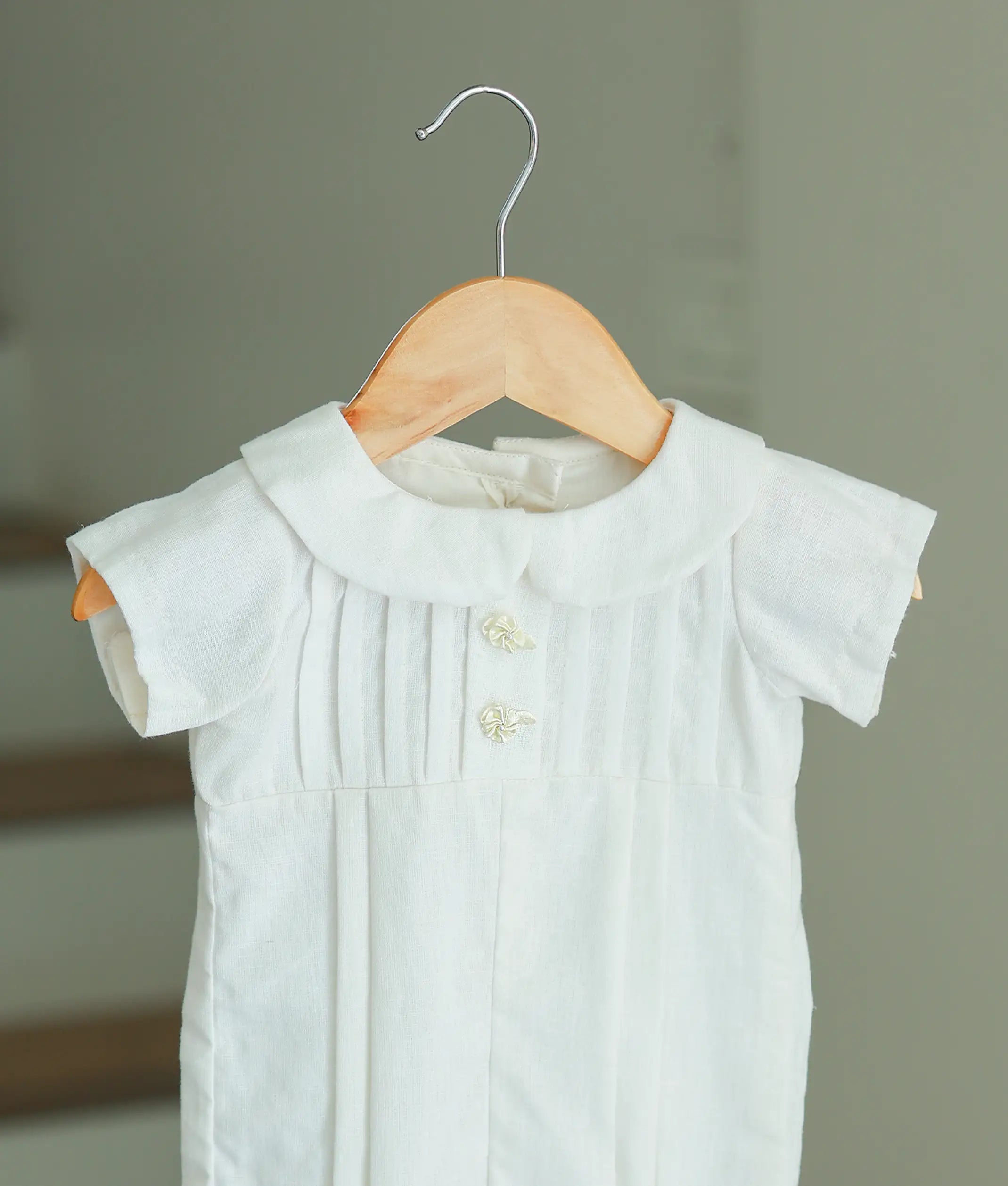 Close-up of the baby romper's bodice showing the intricate vertical pleating, Peter Pan collar, and delicate floral button accents