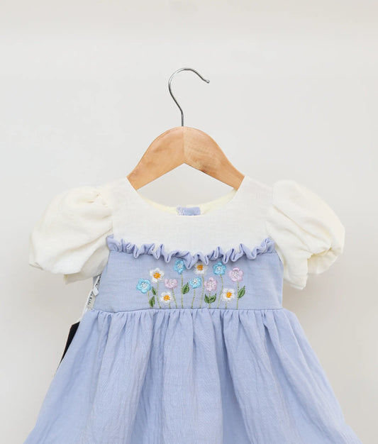 Close-up of the delicate floral embroidery and flared skirt lace trim on the blue linen dress