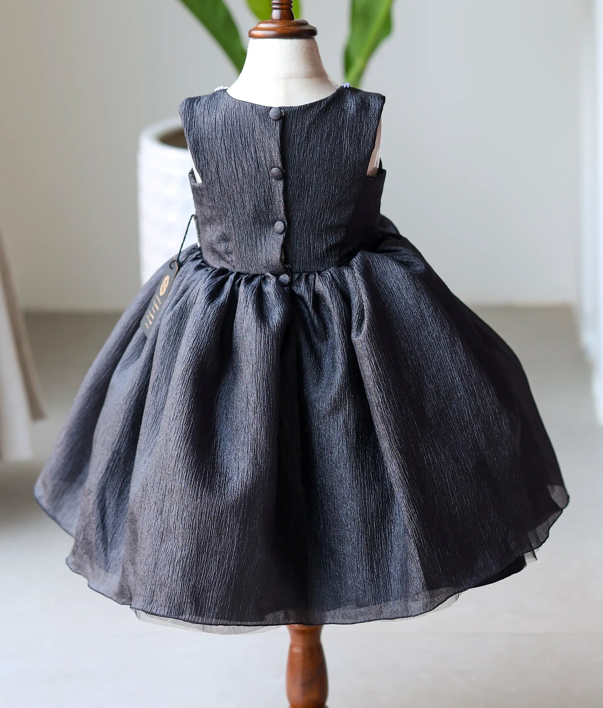 Back view of black crush organza frock showing the round neckline with show button and the full multiple-layered skirt