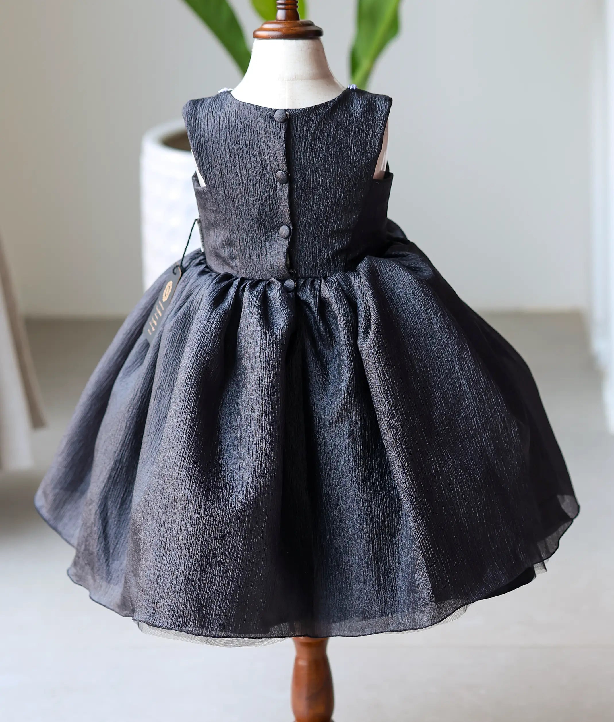 Back view of black crush organza frock showing the round neckline with show button and the full multiple-layered skirt