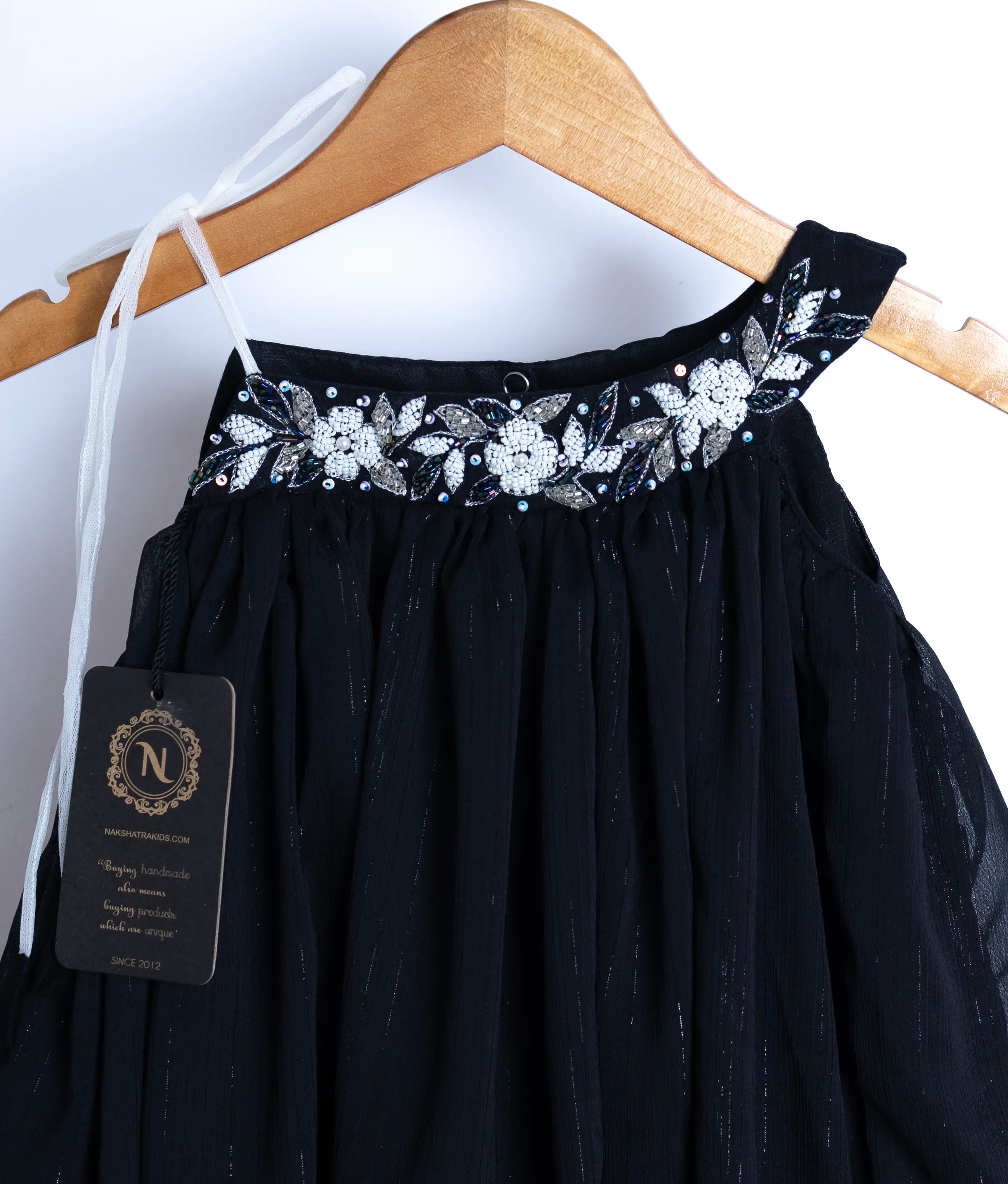 Close-up of the black dress showing detailed white floral embroidery, pearls, and beads on the neckline