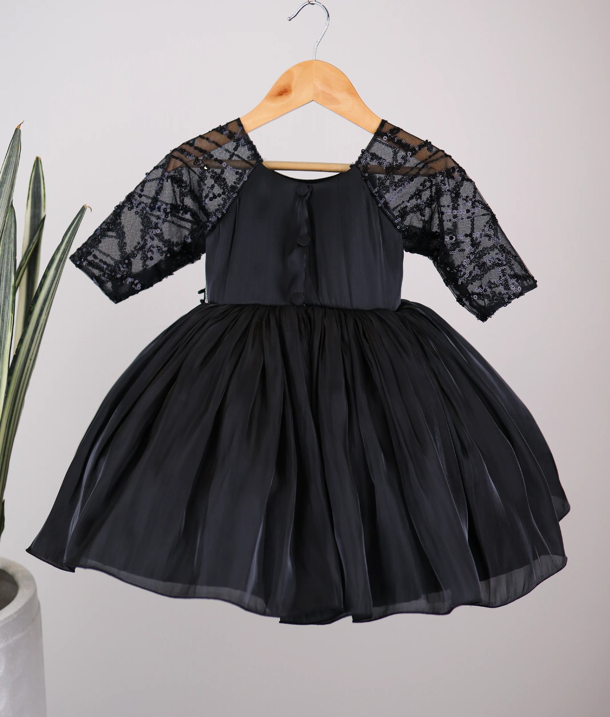 Back view of black lacer organza dress showing the round neckline with show button and the elegant flared below-knee skirt