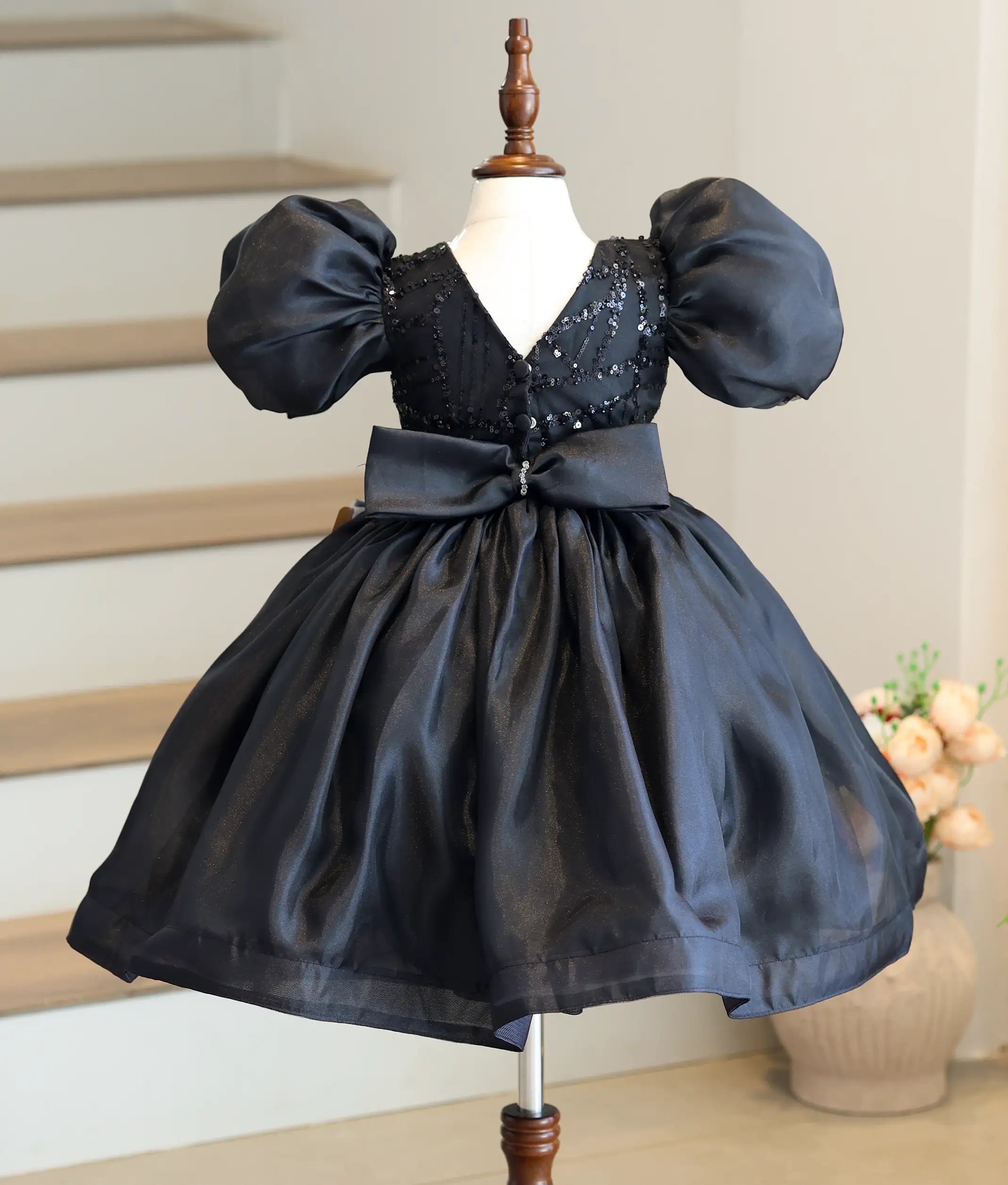 Back view of the black frock showing the elegant V-neck design and a large decorative crystal bow