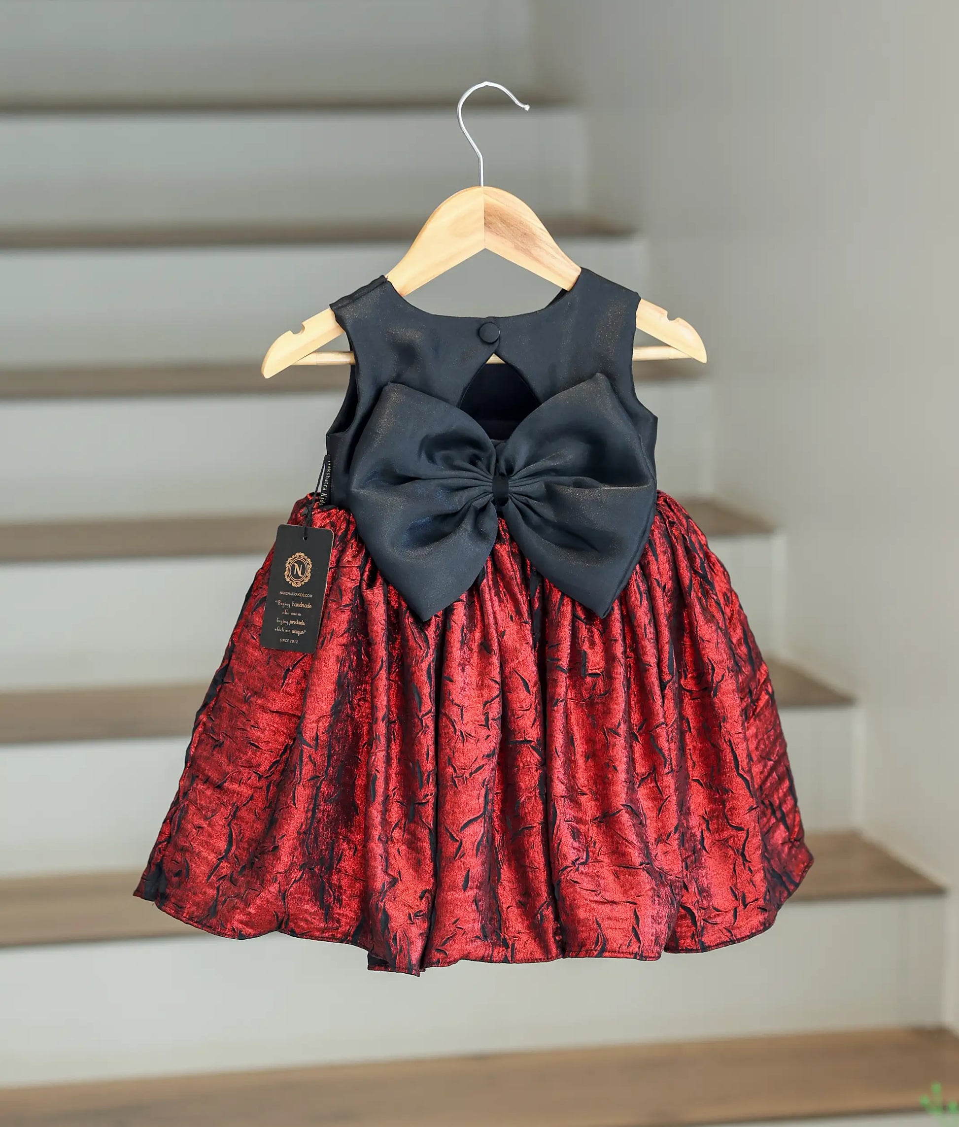 Back view of the baby girl's frock showing the round neck, show button, and large black decorative bow.