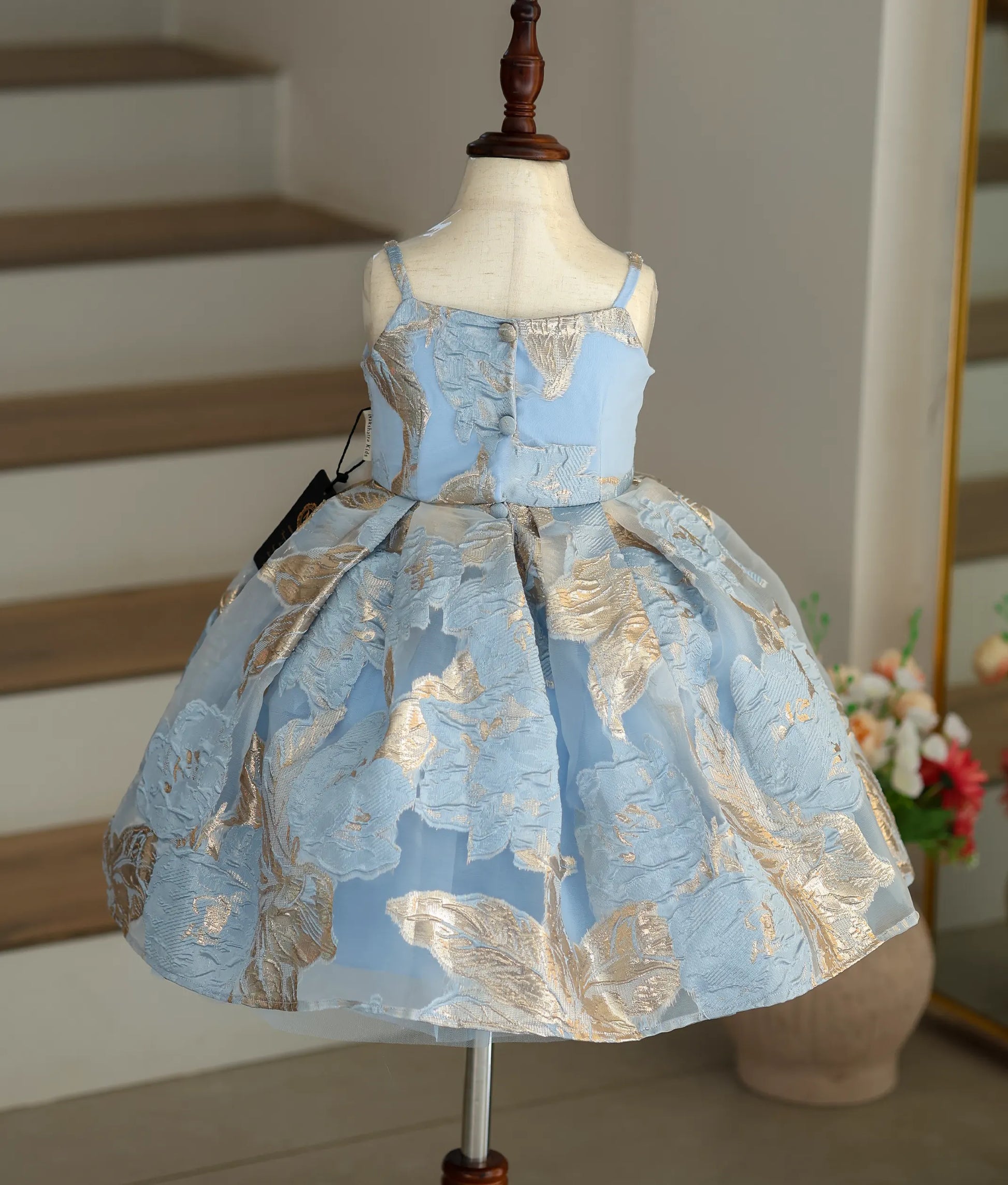 Back view of the blue frock showing the pleated flair and button closure.
