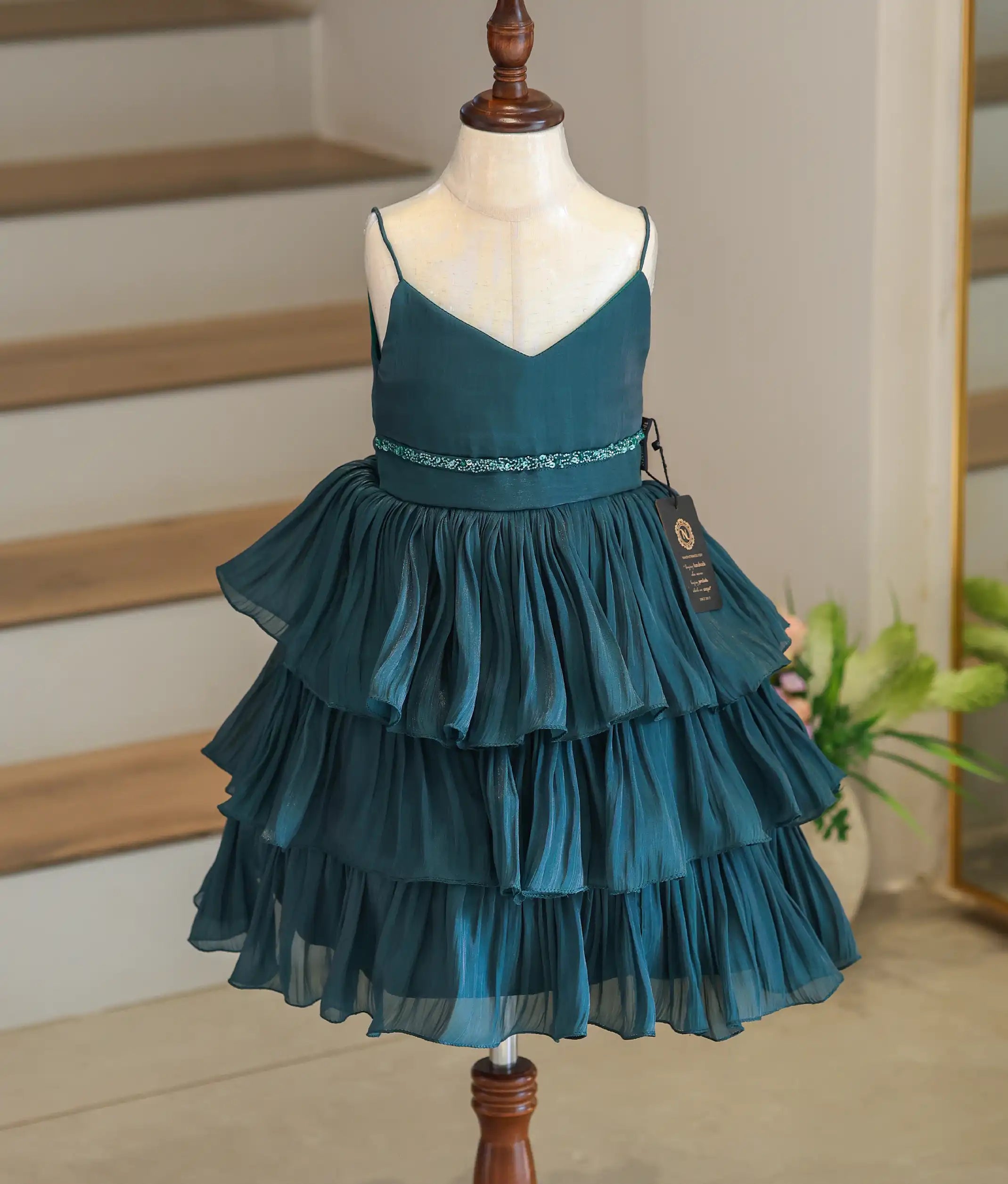 Front view of a bottle green tiered frock for girls made of shimmery laser organza with a handworked waistline.