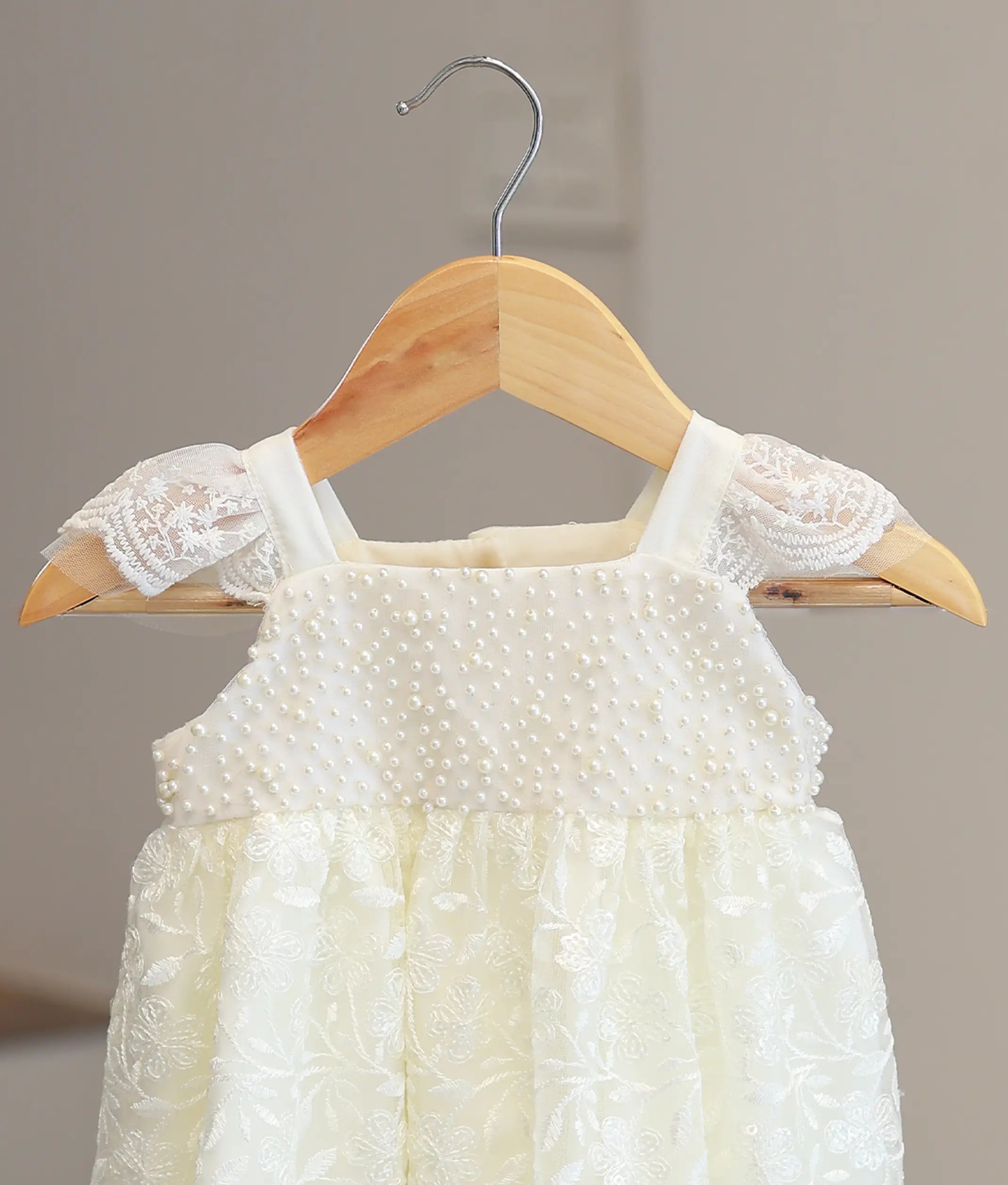 Close-up of premium hand-stitched pearl accents and fine lace detailing on a handcrafted off-white baptism dress