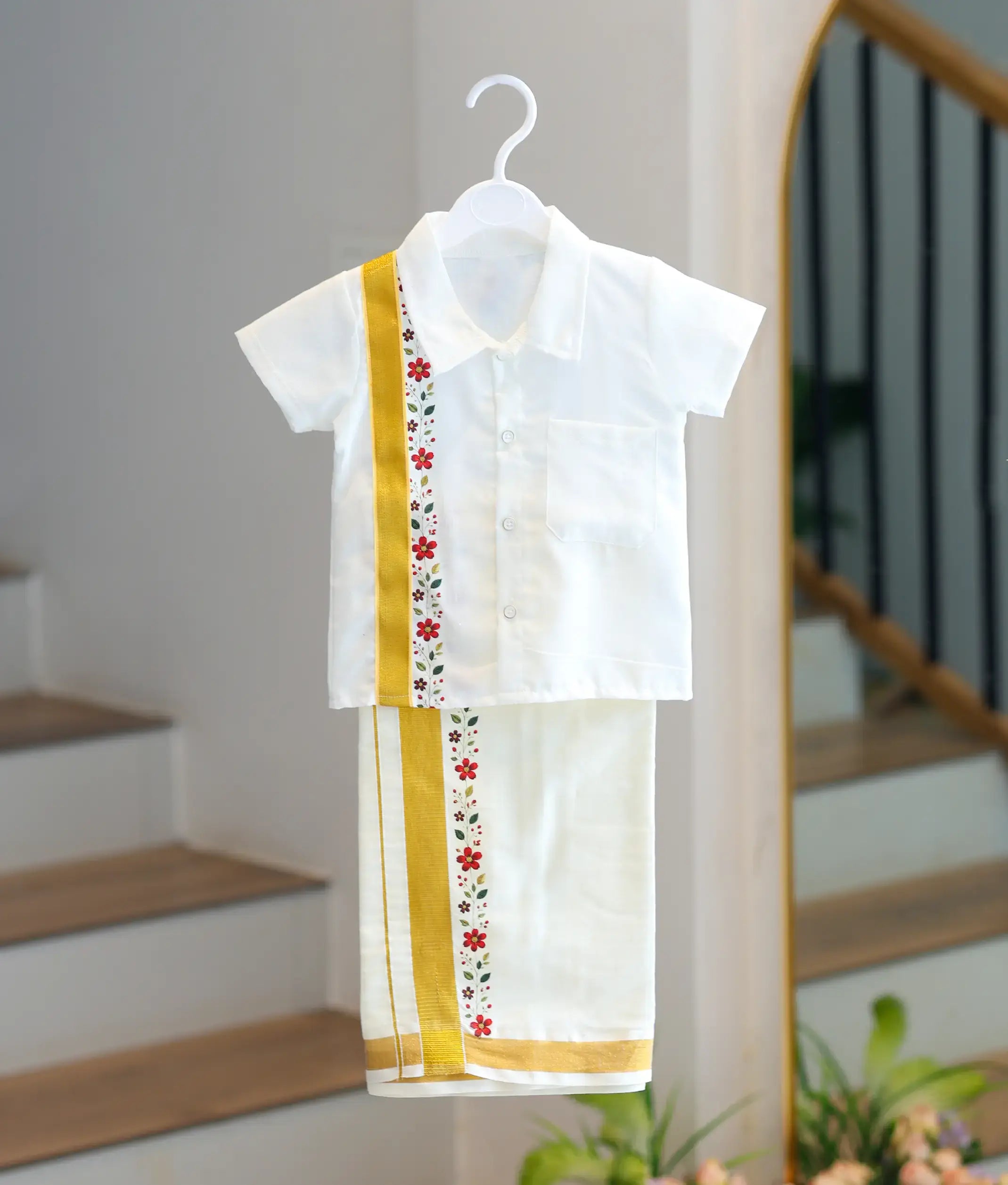 Studio display of the boys off-white cotton shirt and matching gold border mundu set on a white hanger.