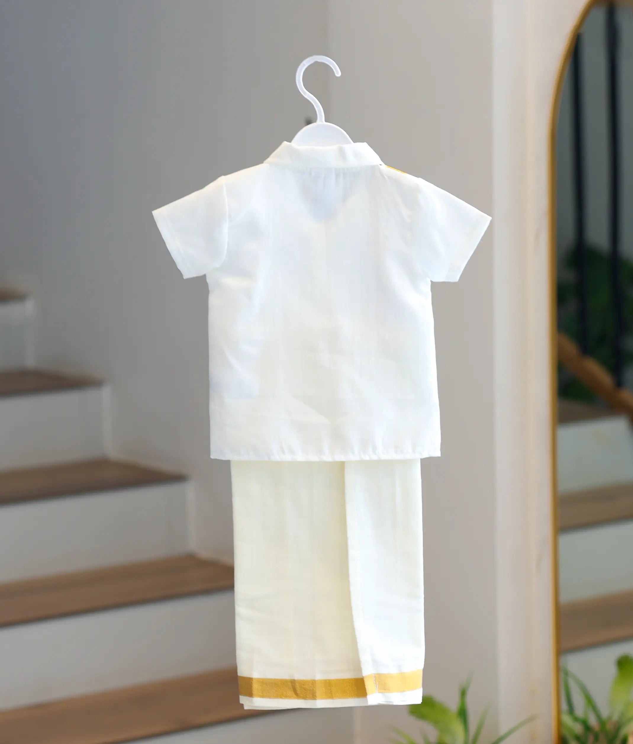 Back view of the boys short-sleeved plain off-white cotton shirt and mundu set.