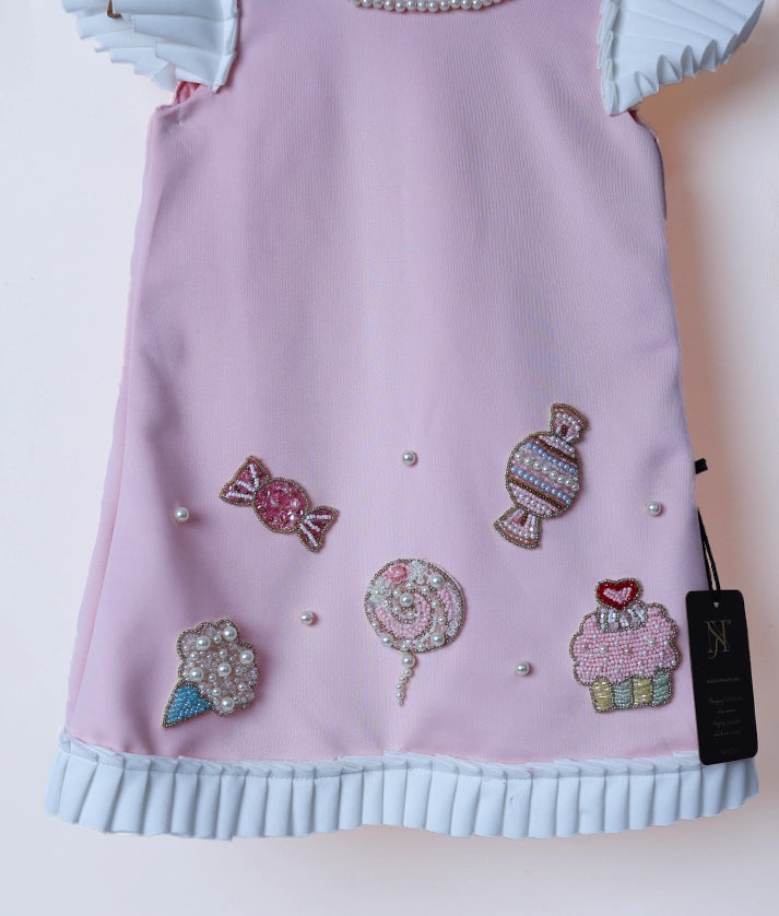 Close-up of the candy-themed hand embroidery and soft baby pink scuba fabric on the birthday frock