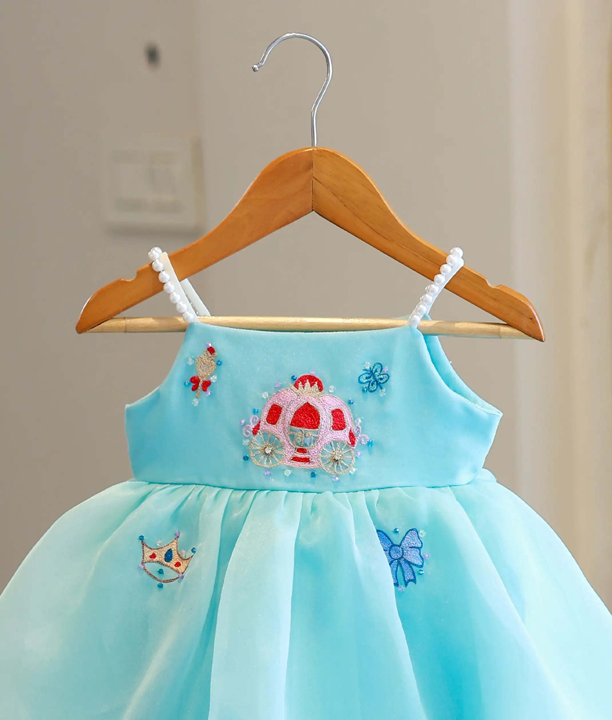 Close-up of the handworked Cinderella carriage motif and pearl-beaded straps on the sky blue birthday gown