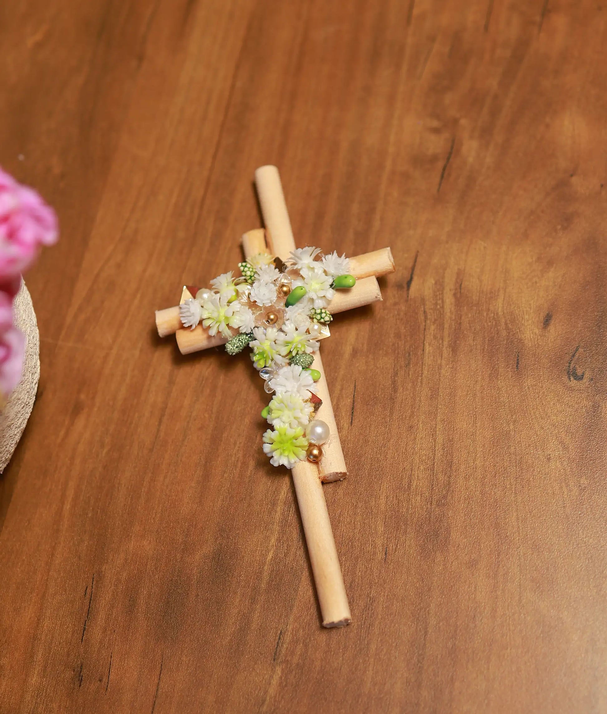 Close-up of showing detailed white and green flowers, gold-tone beads, and pearl handwork on a wooden cross