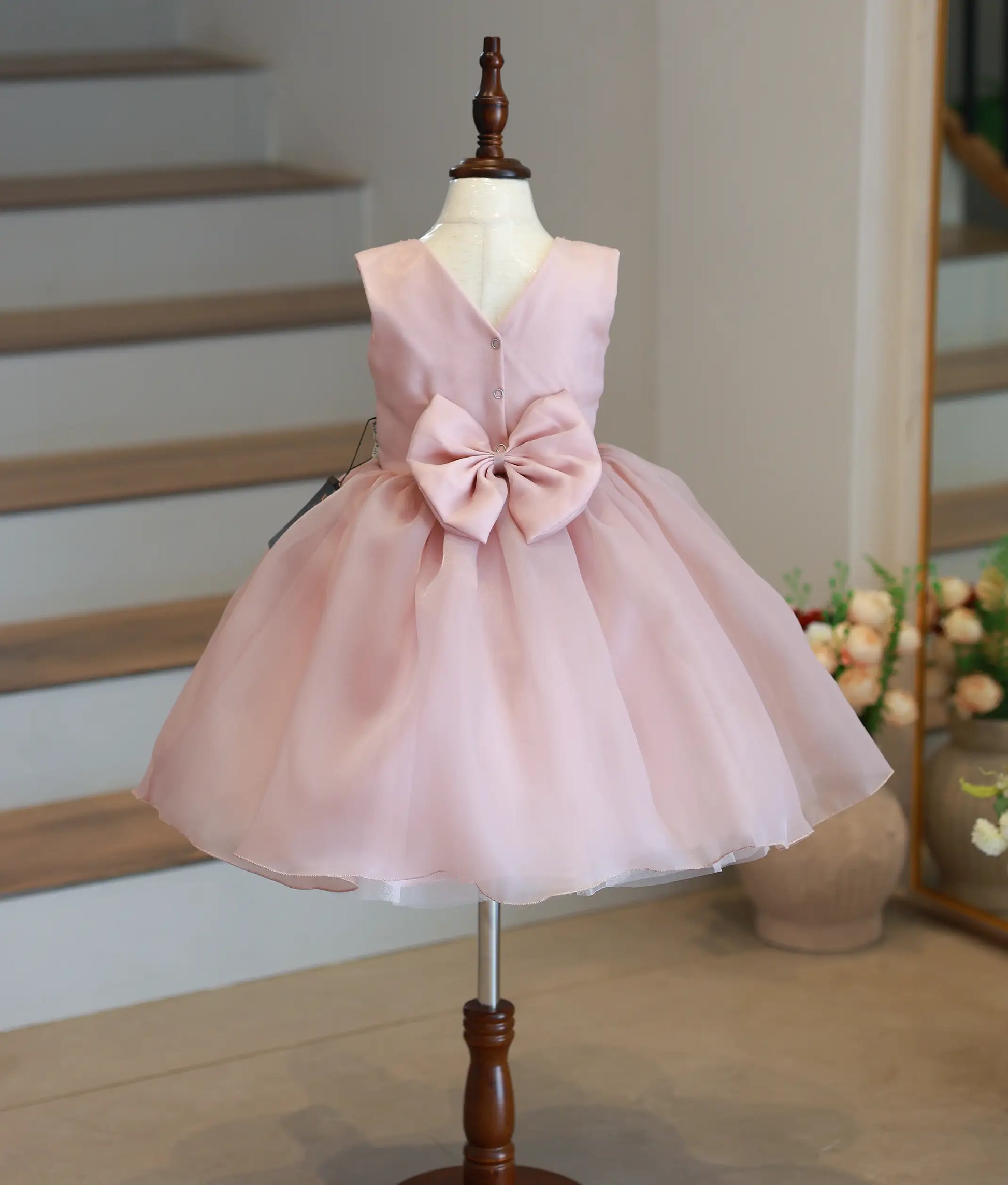 Back view of the beige cartoon theme frock featuring a closed neckline with a show button and a decorative bow.