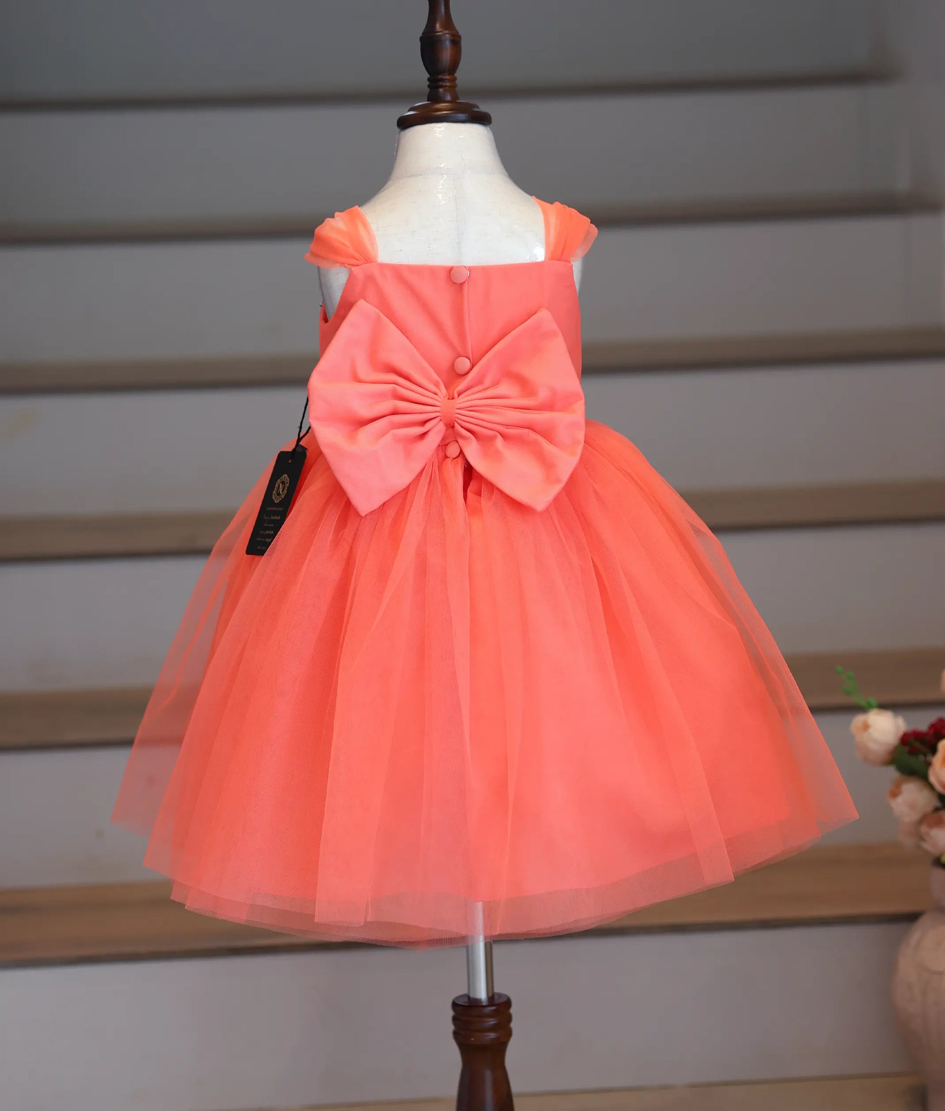 Back view of the coral peach frock showing the large bow and button closure.