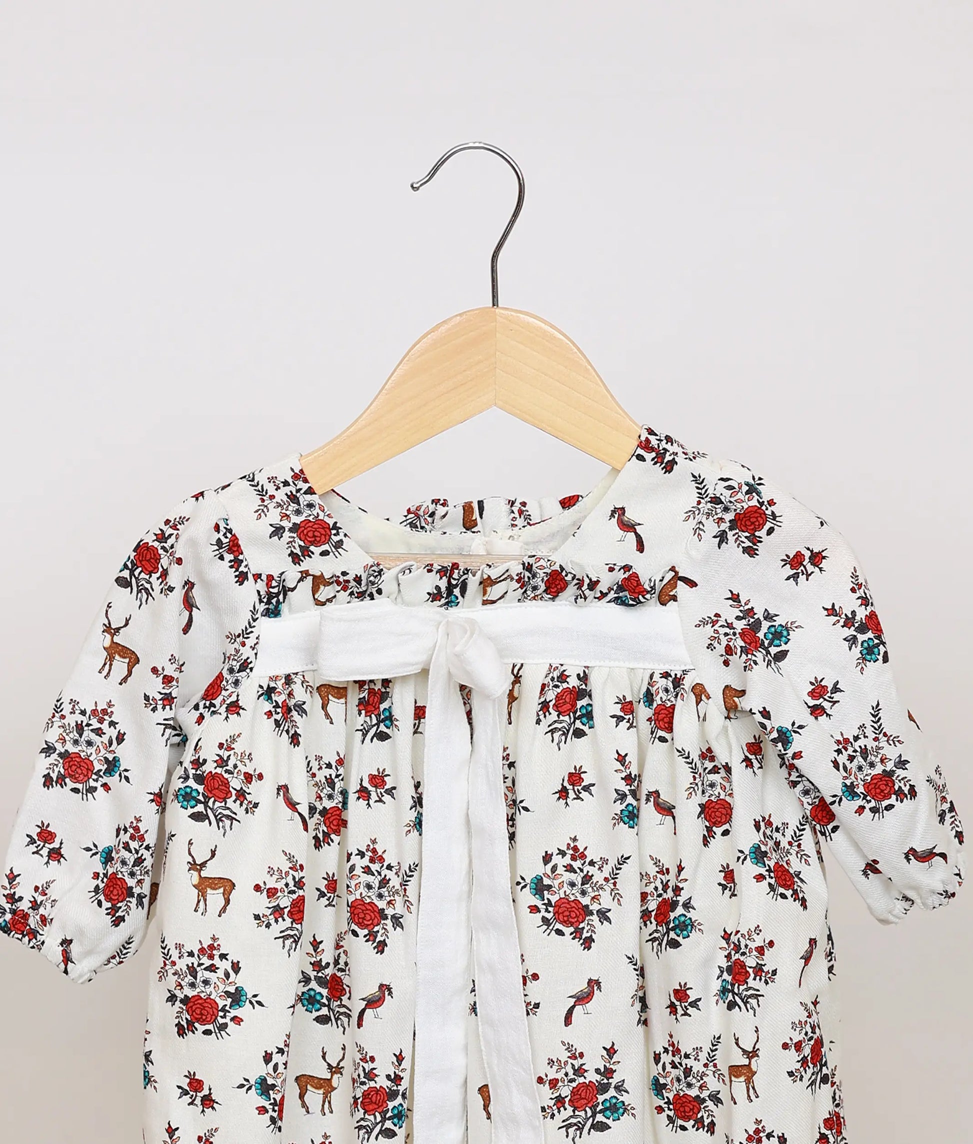 Close view of white cotton baby frock yoke, highlighting the red floral and deer print and the central white ribbon tie detail.