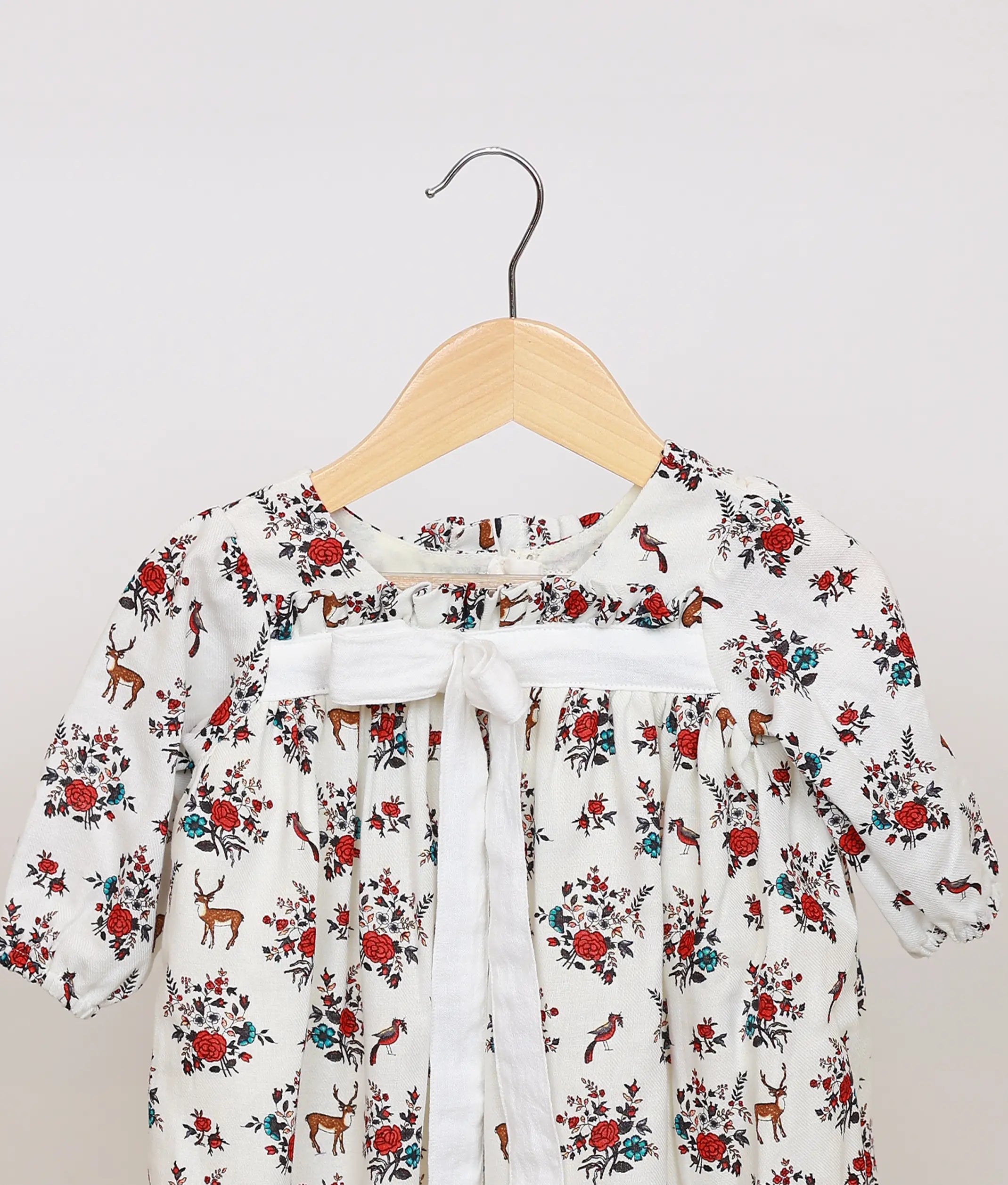 Close view of white cotton baby frock yoke, highlighting the red floral and deer print and the central white ribbon tie detail.
