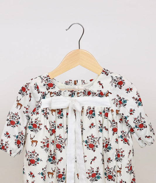 Close view of white cotton baby frock yoke, highlighting the red floral and deer print and the central white ribbon tie detail.