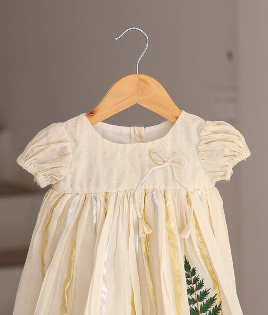 Close-up of the short puff sleeves, gold-striped bodice, and delicate tassel tie on the off-white baby dress