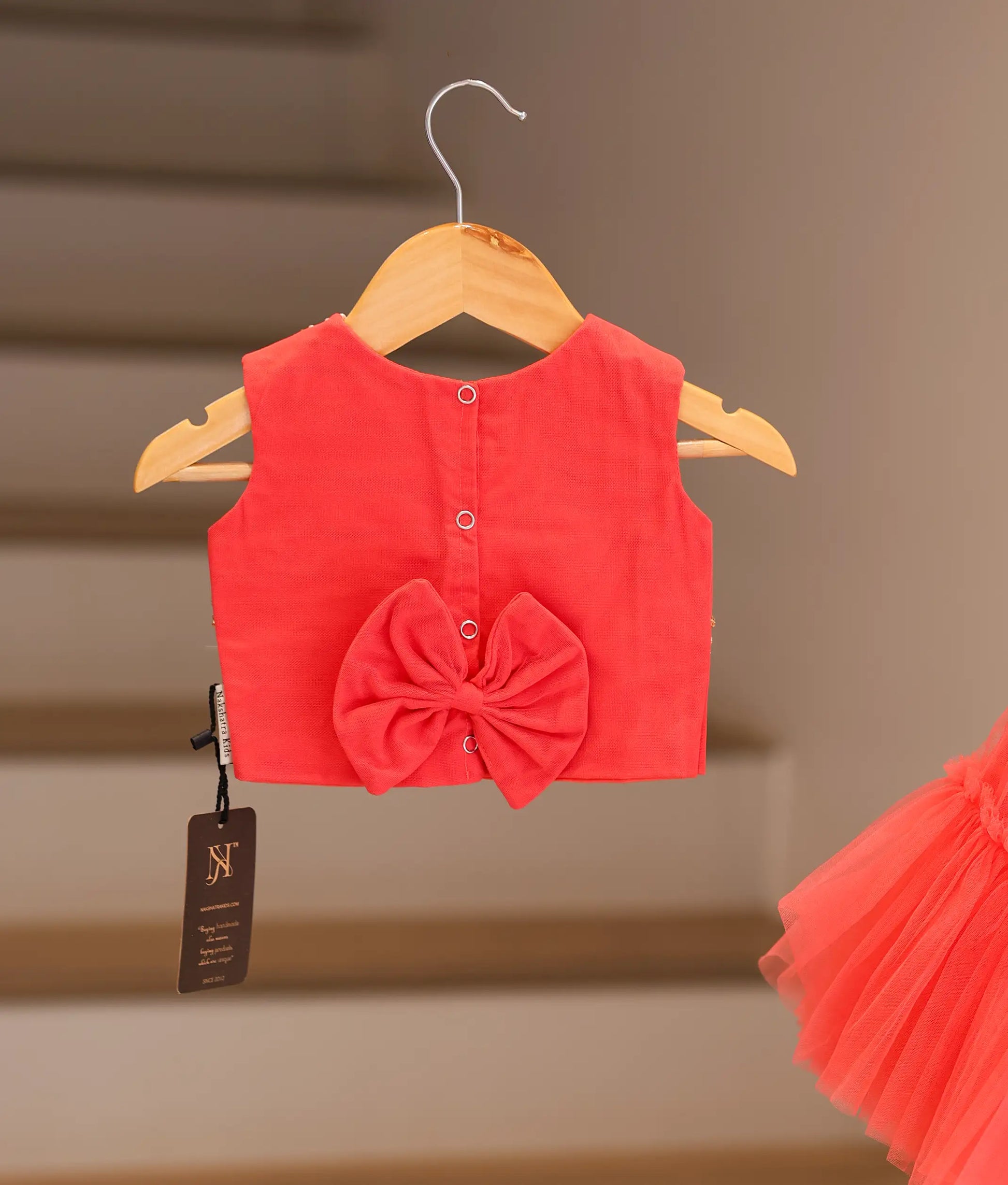 Back view of the dark pink crop top and skirt showing the round neck, press button closure, and decorative bow