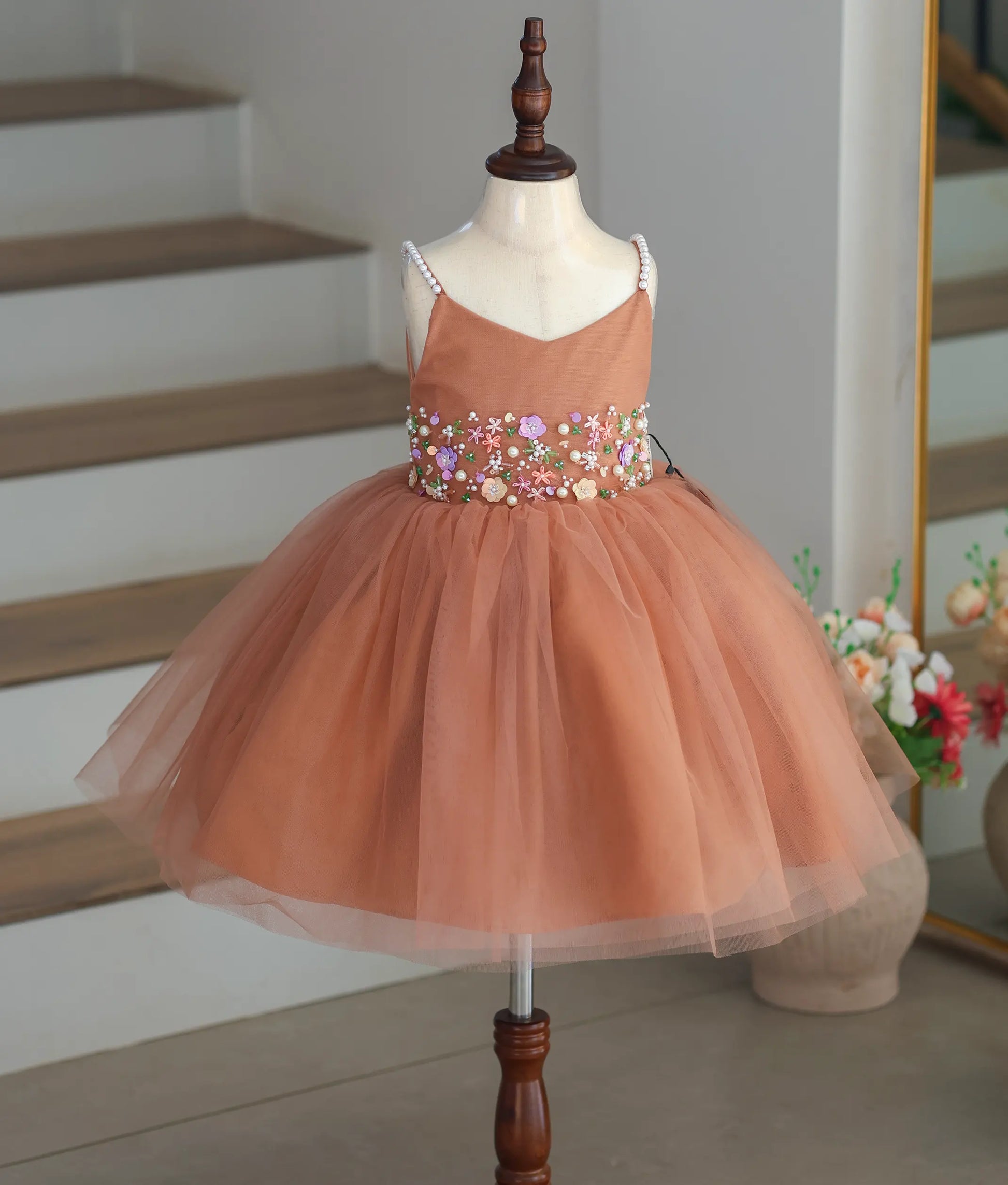 Front view of a dusty peach frock for girls with floral handwork and pearl straps.