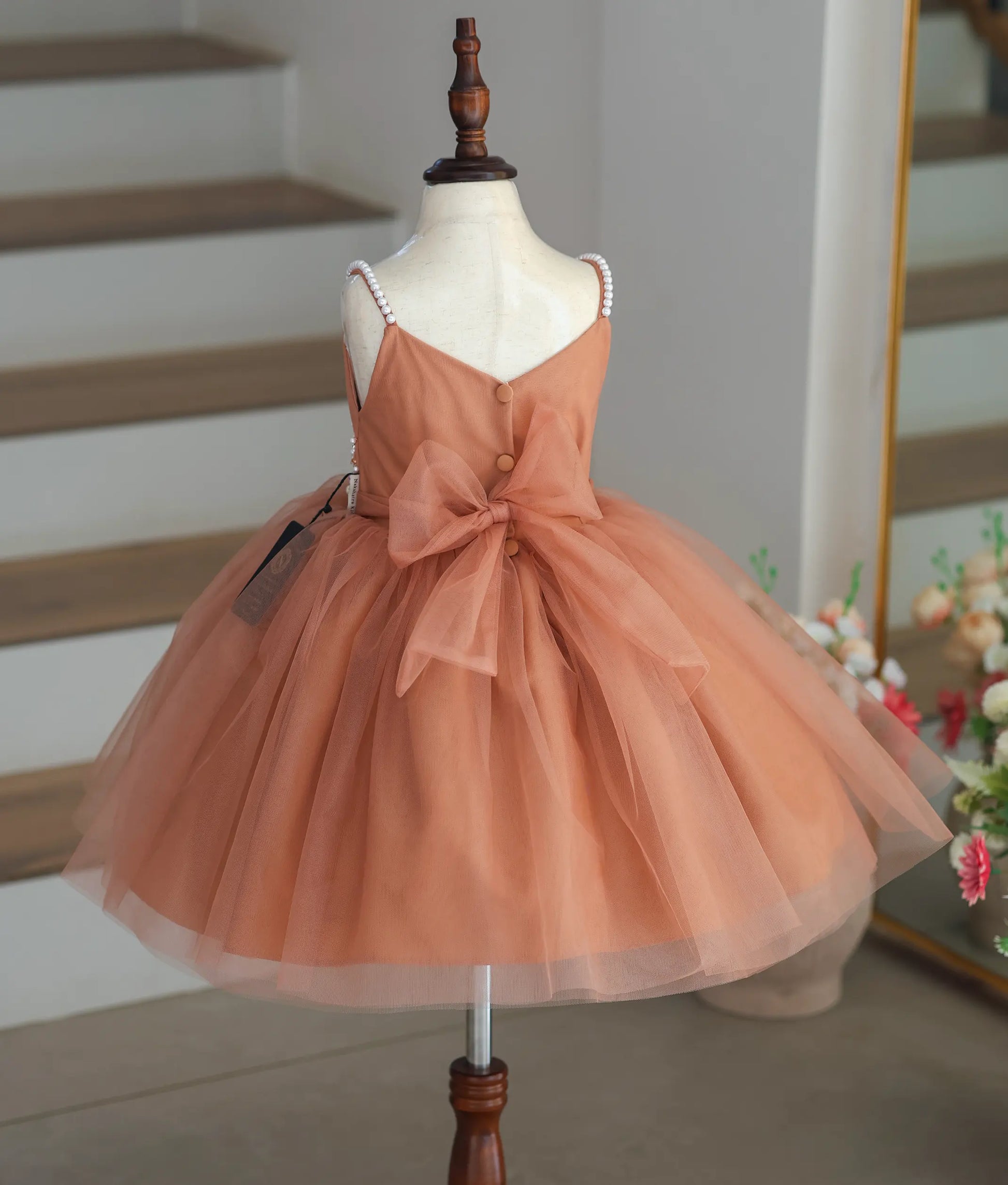 Back view of the dusty peach frock showing the V-neck cut and the large tie-back bow.