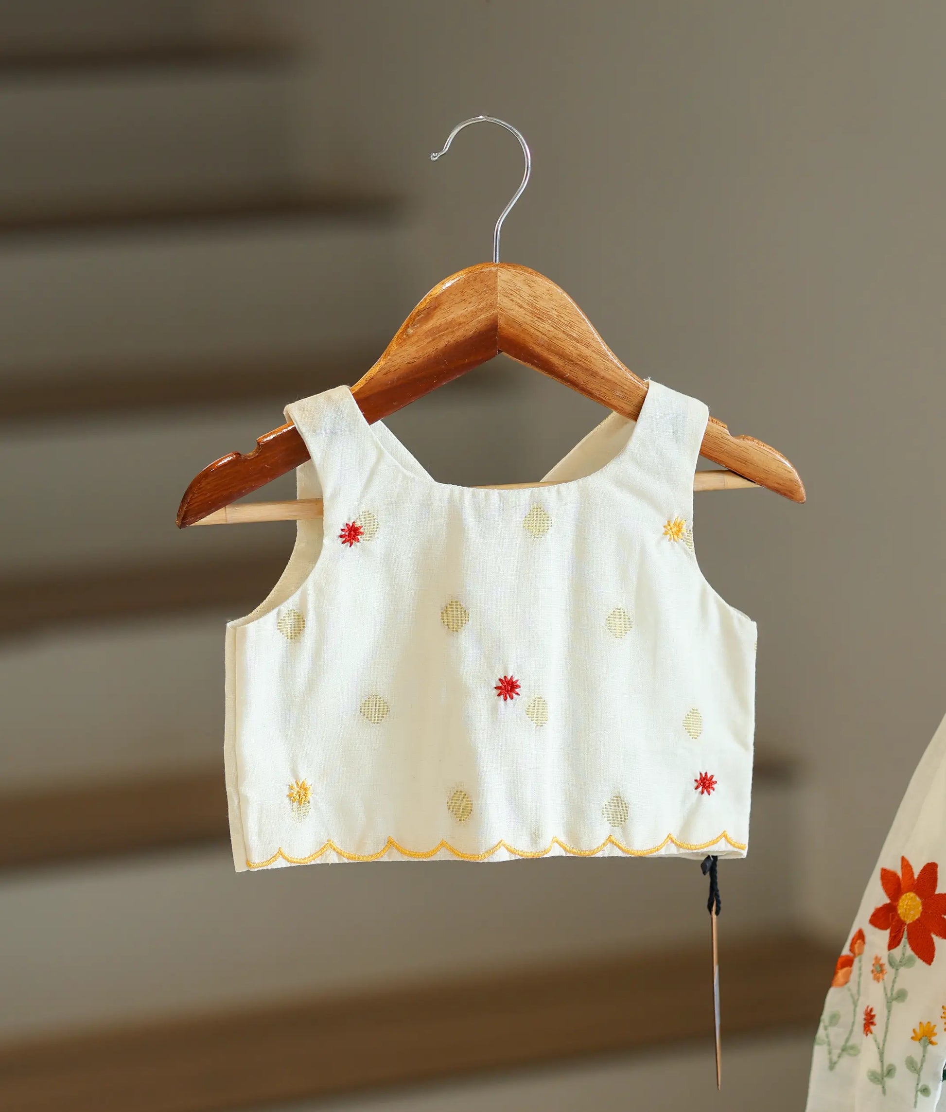 Close-up of the embroidery motifs and scalloped hem on the off-white top.