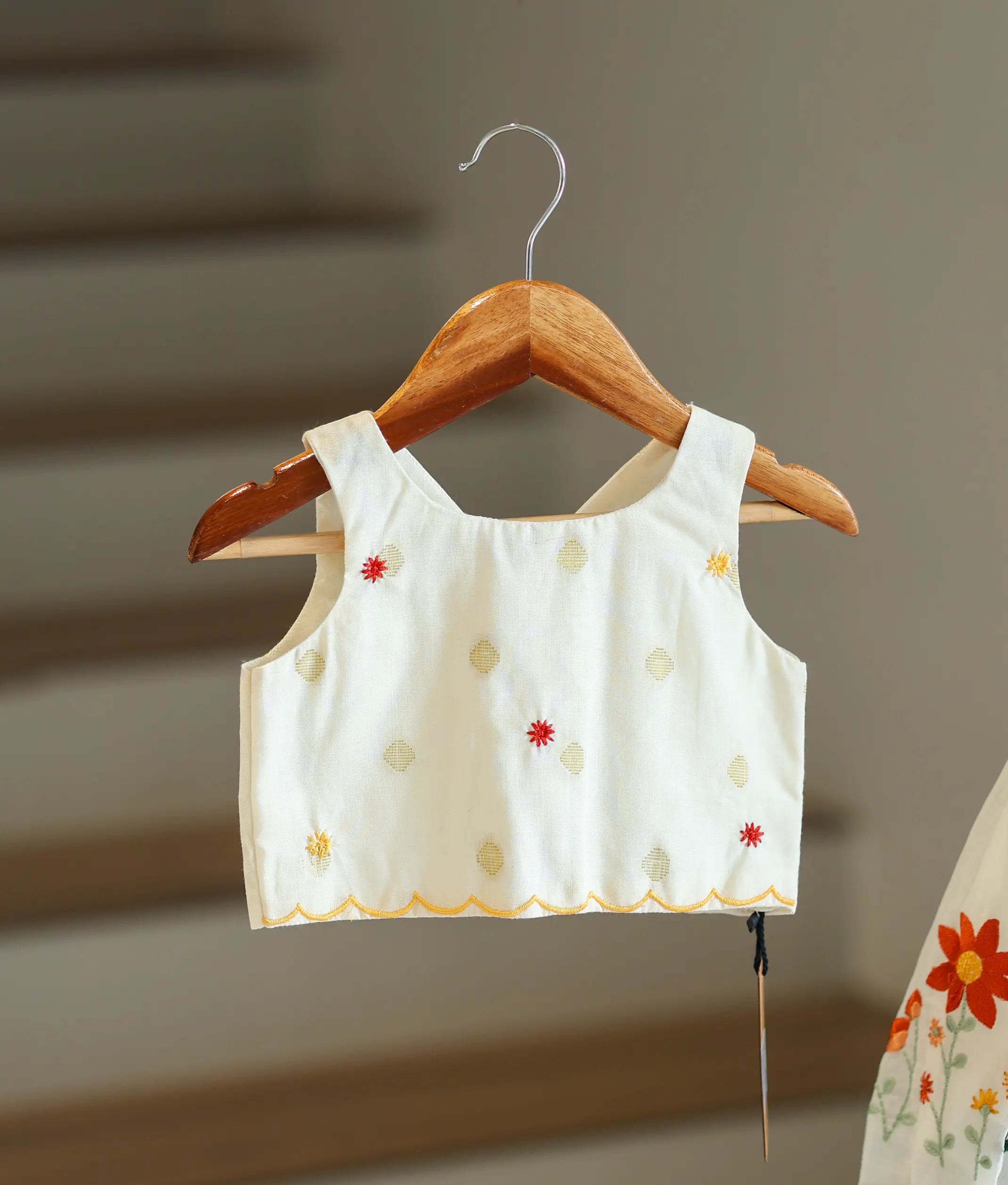 Close-up of the embroidery motifs and scalloped hem on the off-white top.