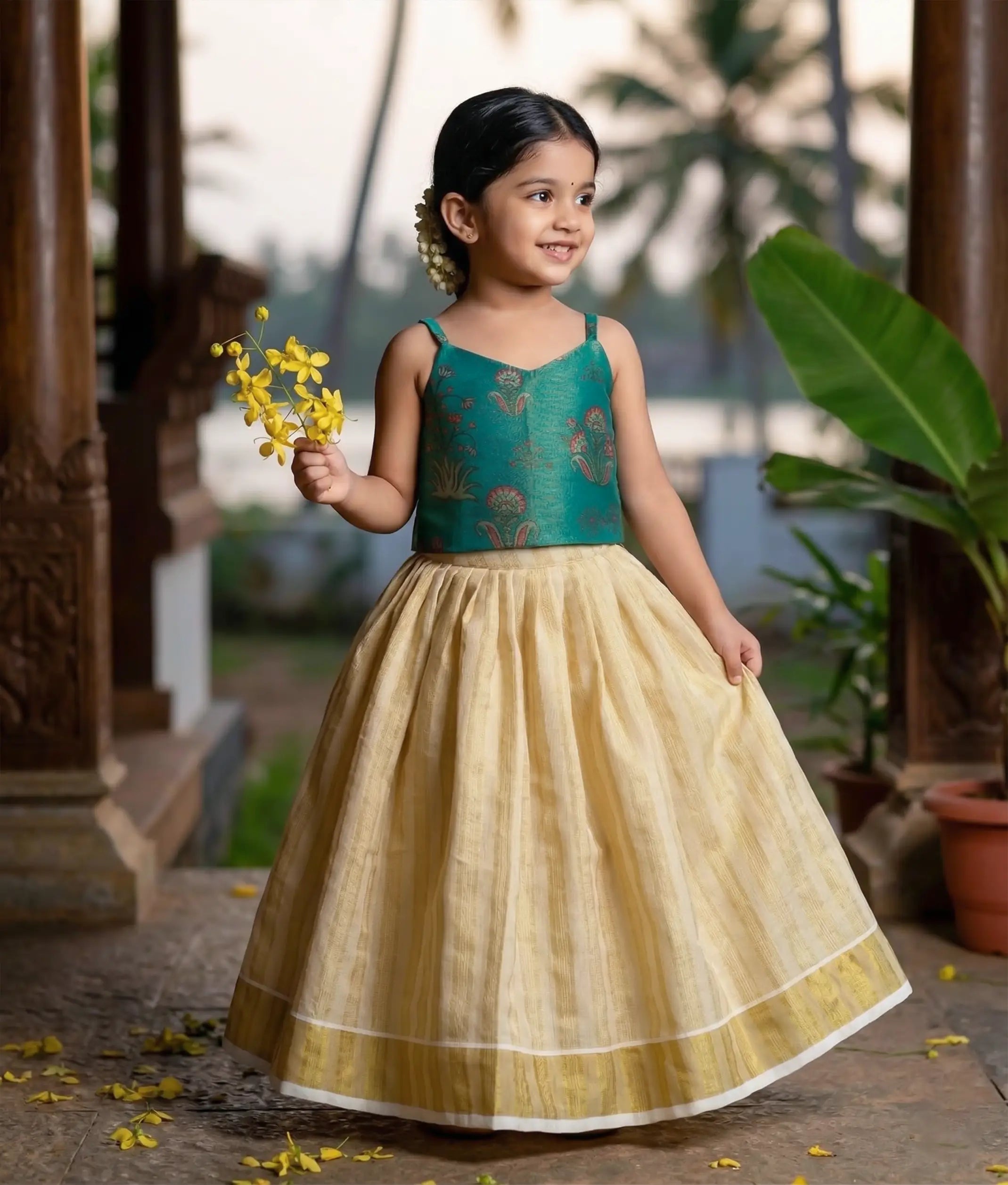 Baby girl wearing emerald green woven top and pleated  kasavu skirt set.