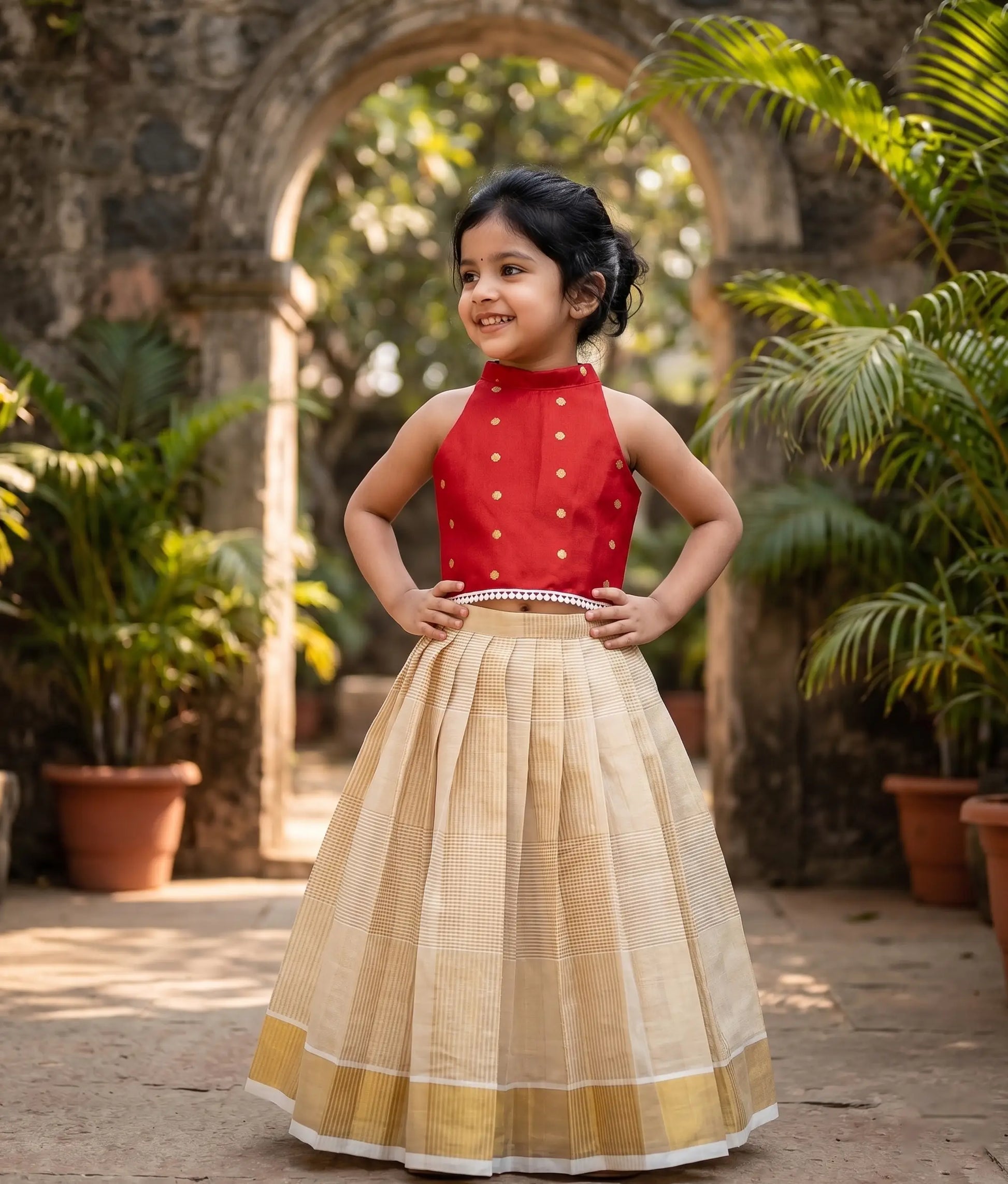 A baby girl wearing a traditional-style red polka-silk top with a kasavu-checked frock.