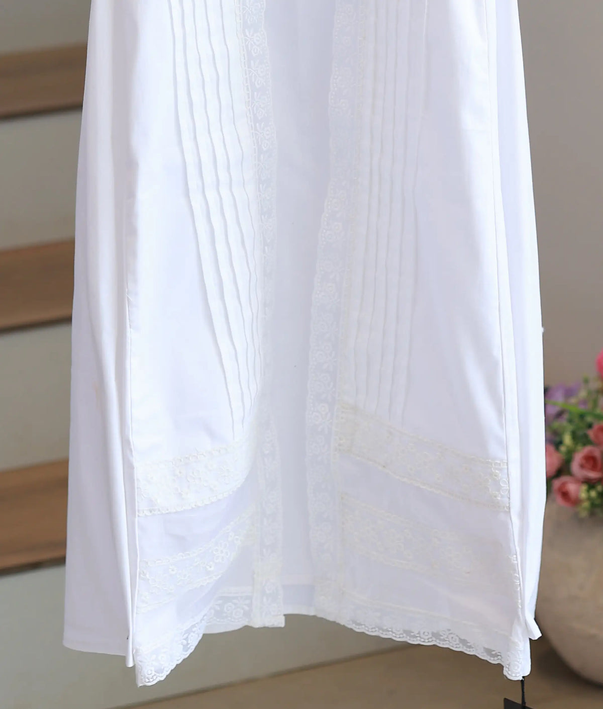 Detailed view of bottom hem on off-white cotton baby boy baptism gown displaying delicate floral lace insertions and pleats.