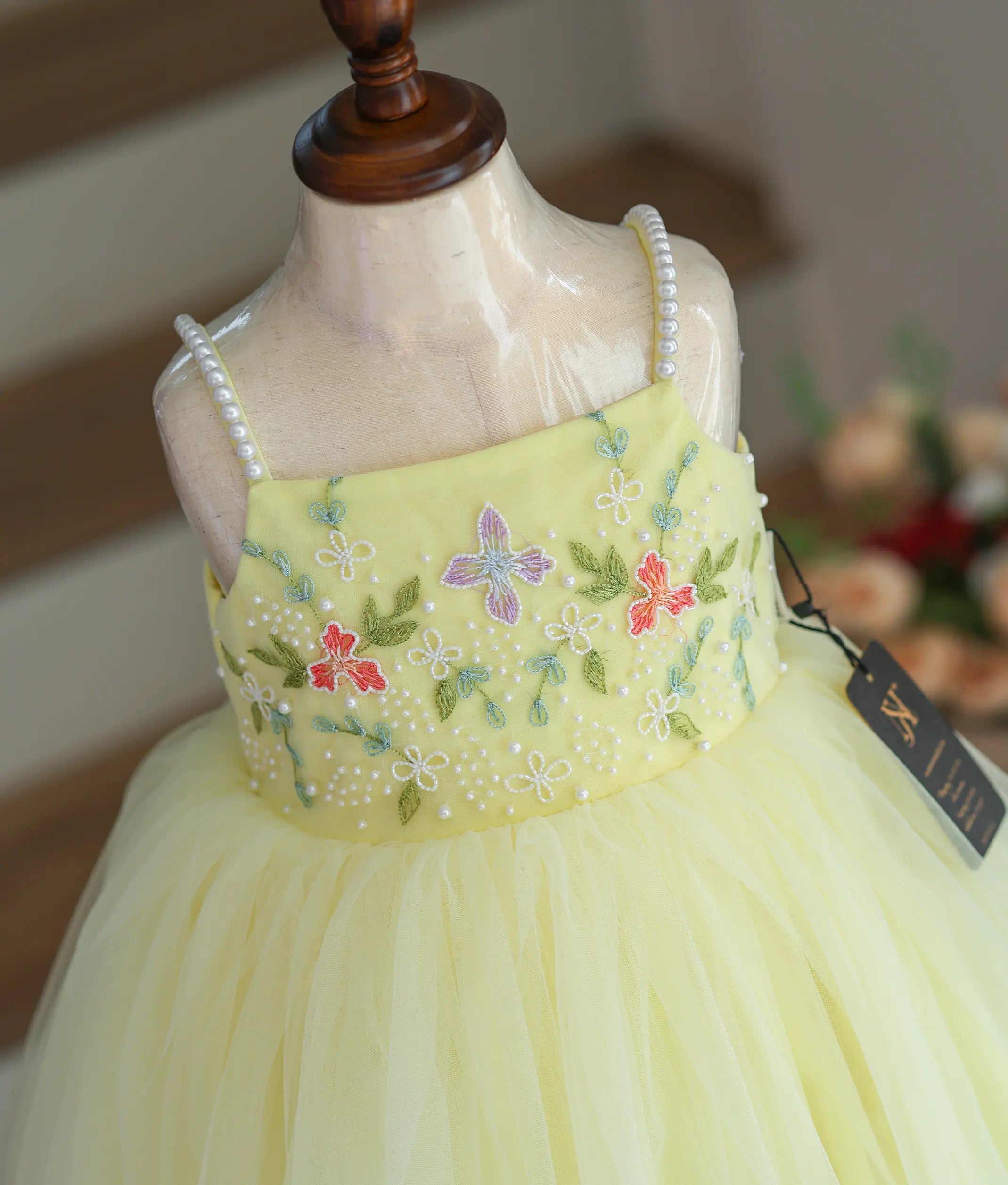 Close-up of the floral handwork, beads, and pearl-decorated straps on the yellow frock.