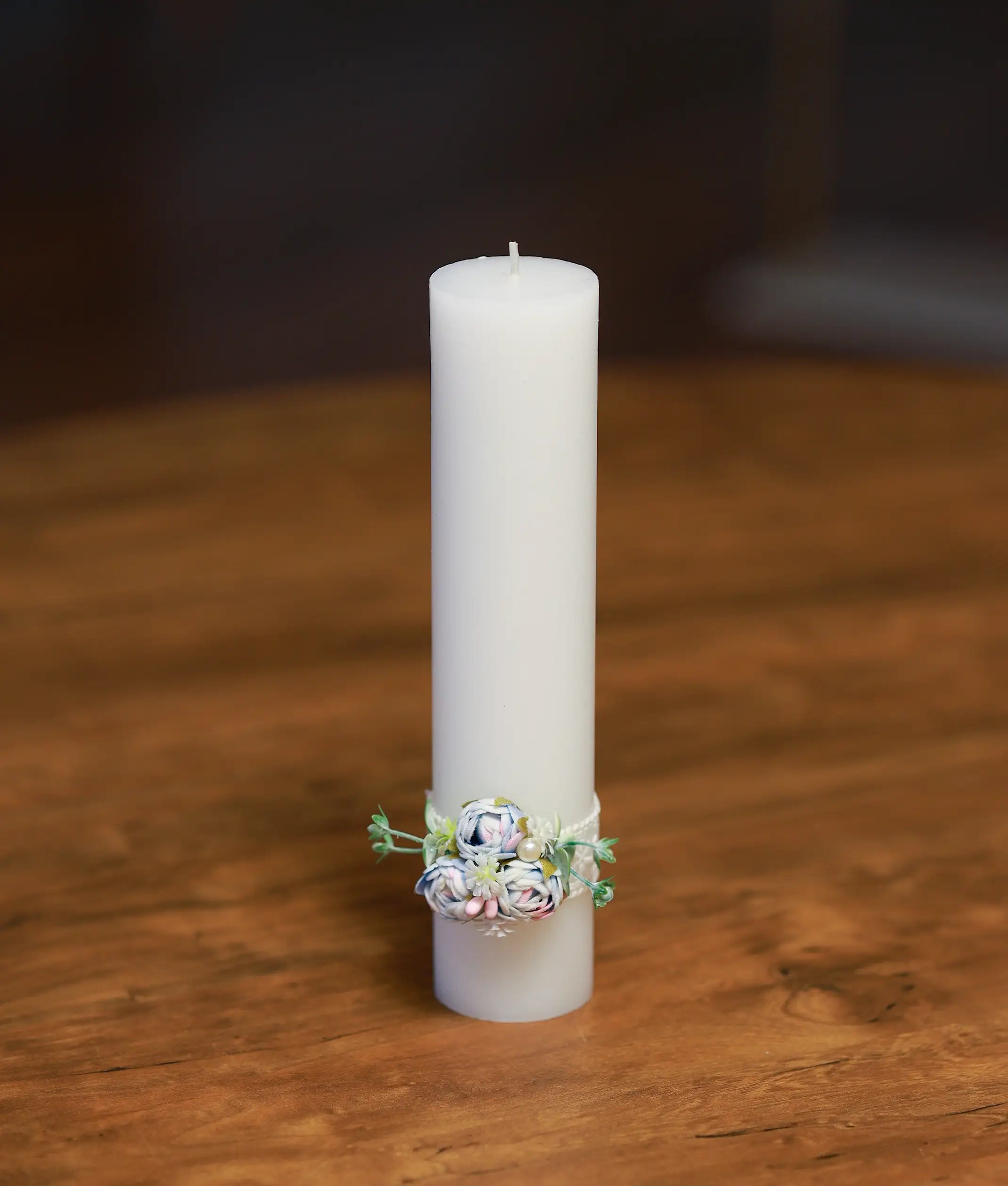Front view of a white decorative baptism candle with a blue and pink floral cluster and white lace band
