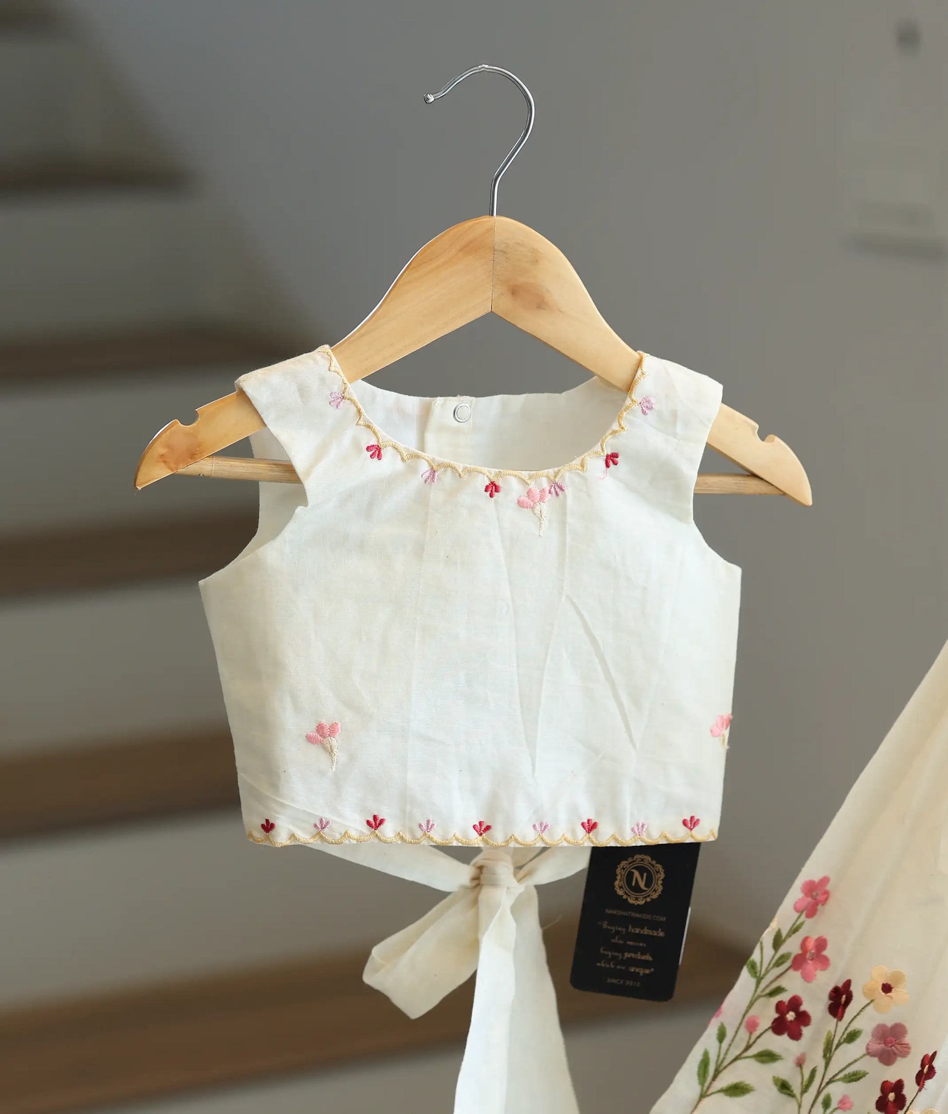Close-up of the pink floral embroidery and scalloped hem on the off-white top.