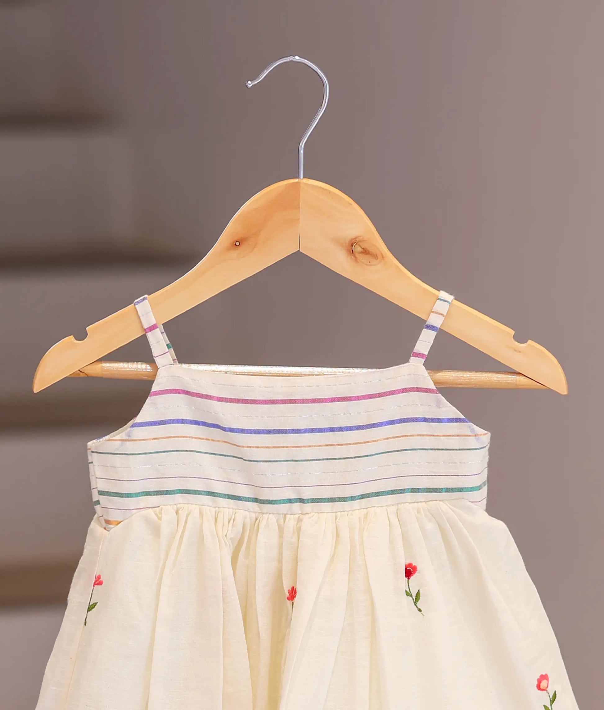 Close-up of the red and pink flower embroidery and the striped strap detail on the off-white cotton fabric.