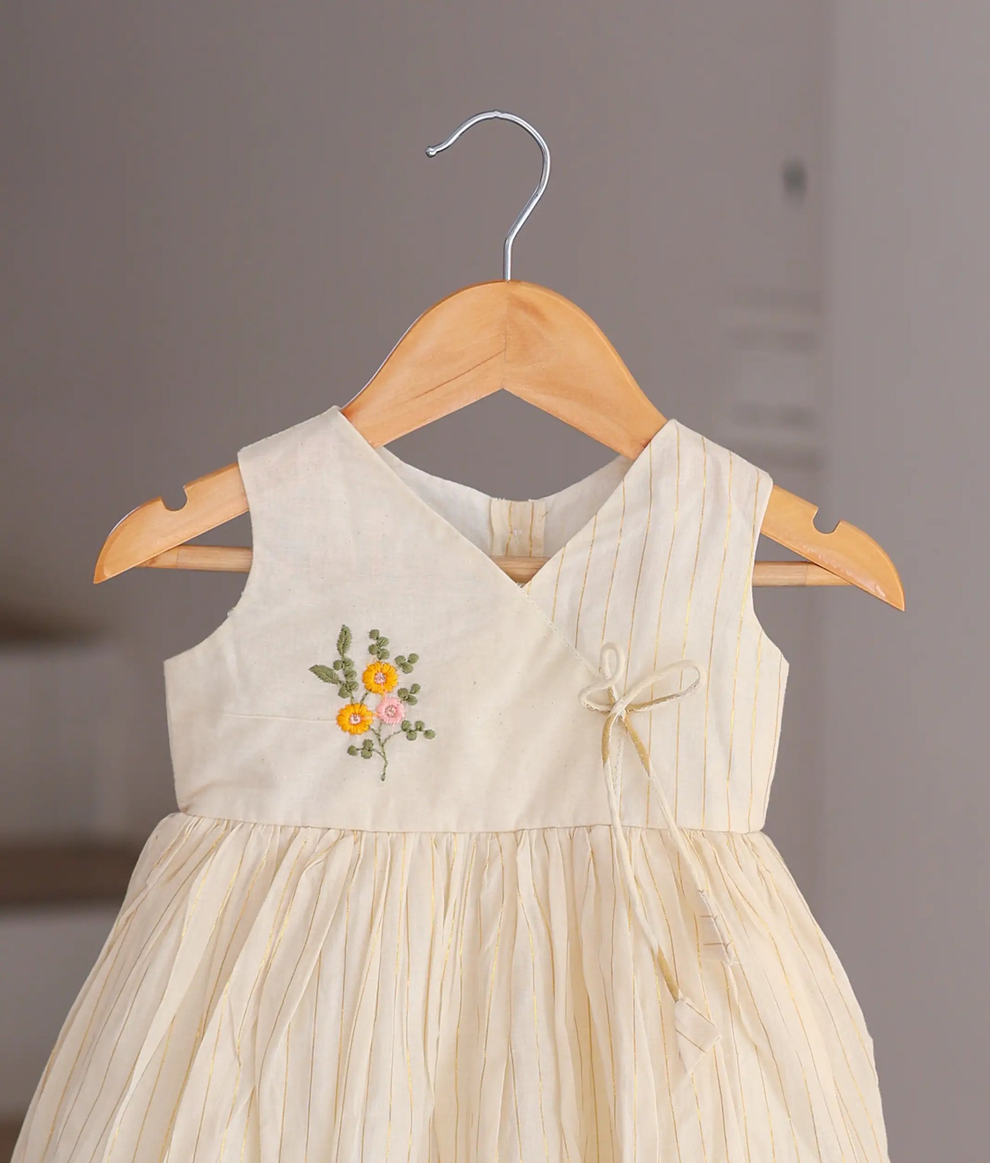 Close-up of the handcrafted pink and yellow flowers and the delicate scalloped hem on the off-white cotton dressv